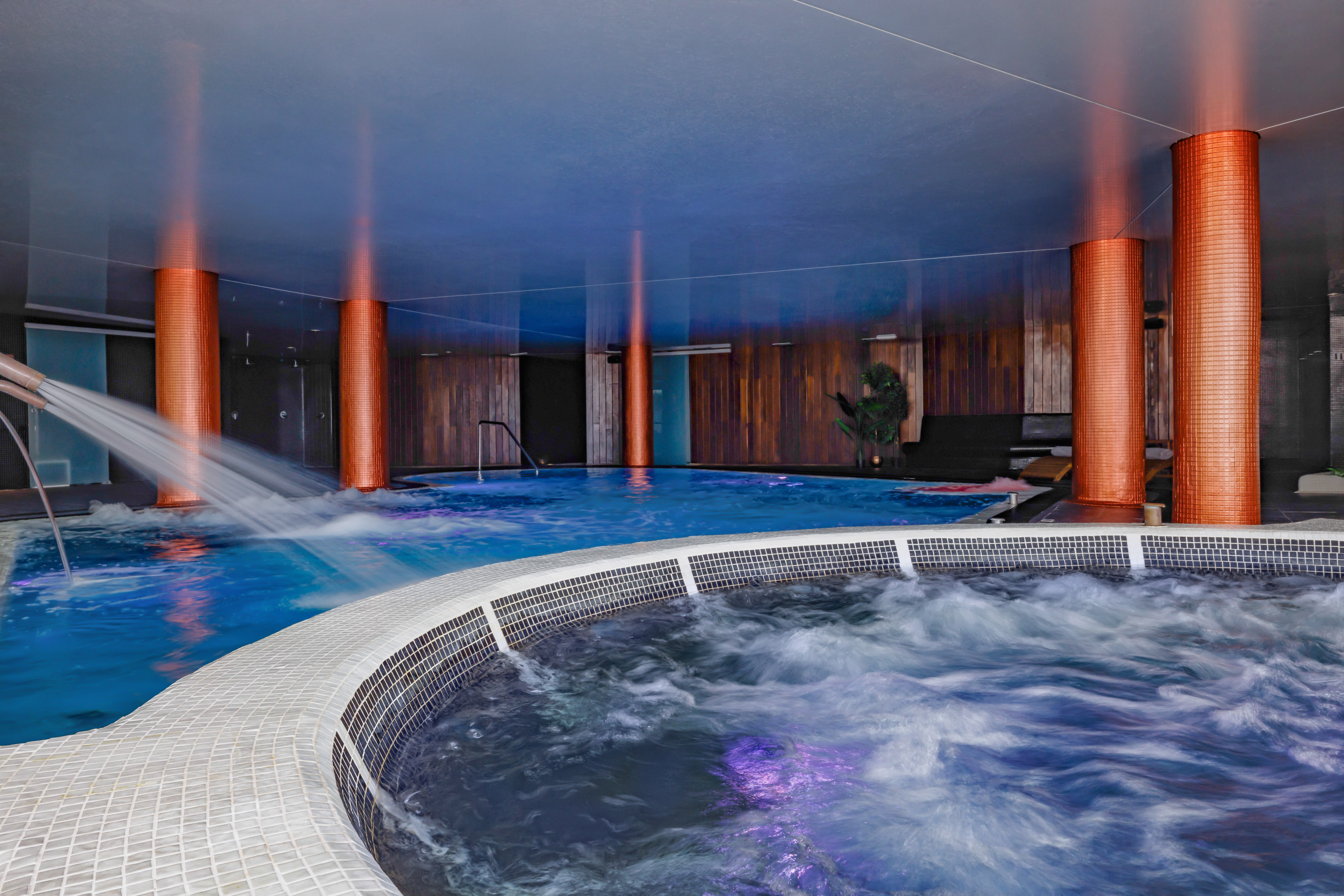 Modern indoor spa with jetted pool, bubbling hot tub, and warm lighting.