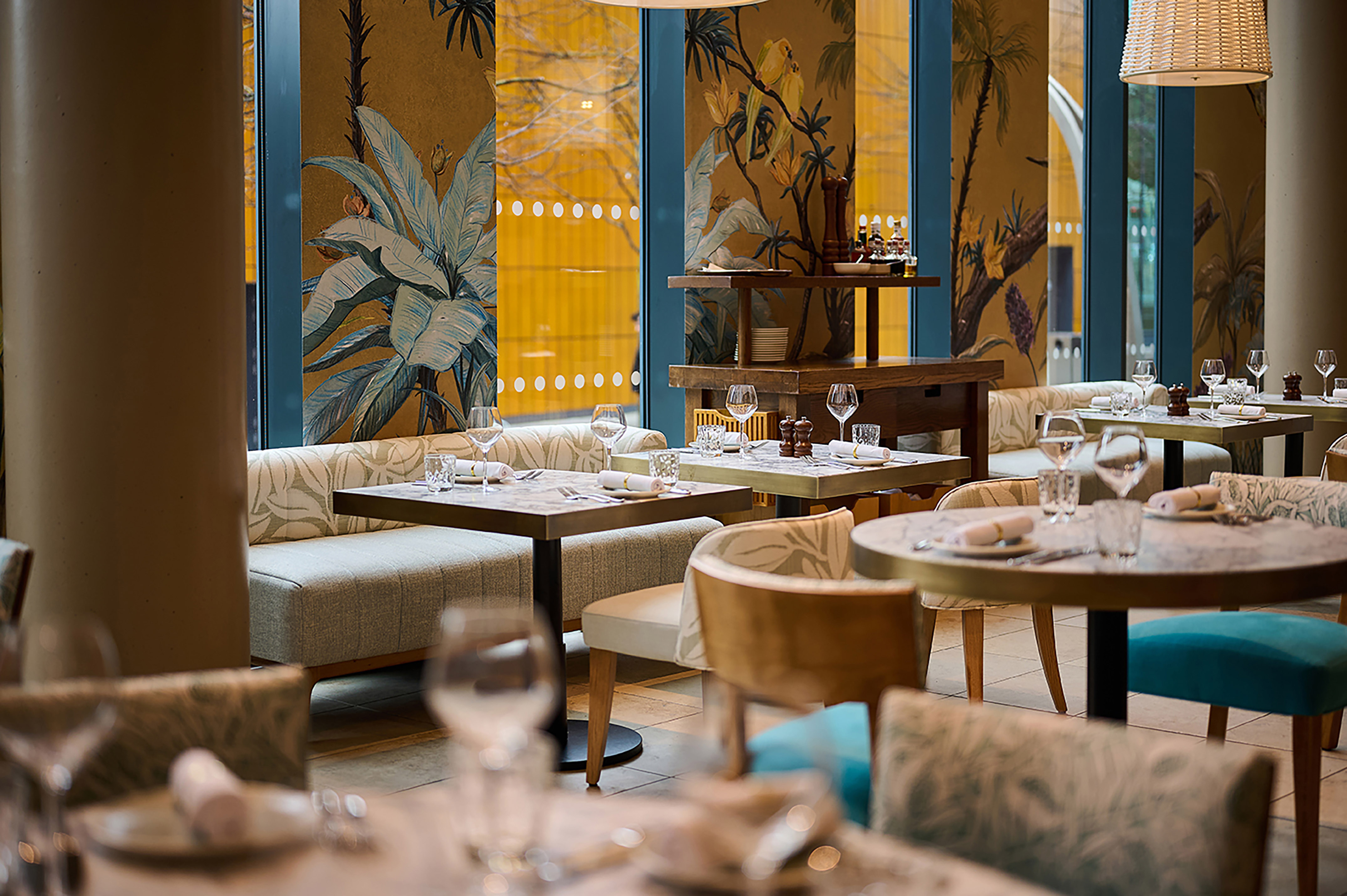 Restaurant dining area with tropical mural, set tables, and banquette seating.
