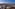 Rooftop bar overlooking illuminated city skyline and mountains at dusk.