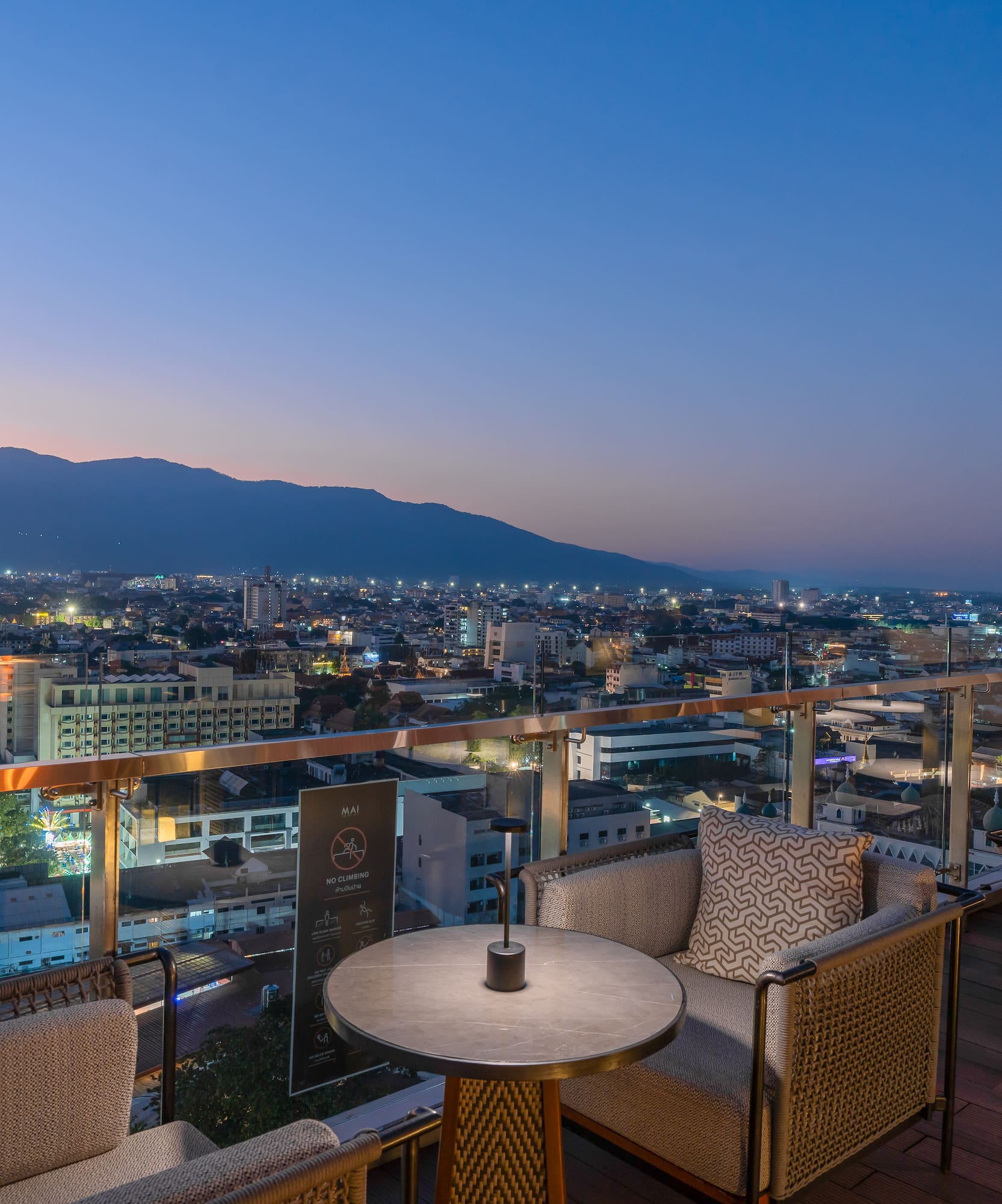 Rooftop lounge with twilight city view, distant mountains, and stylish seating.
