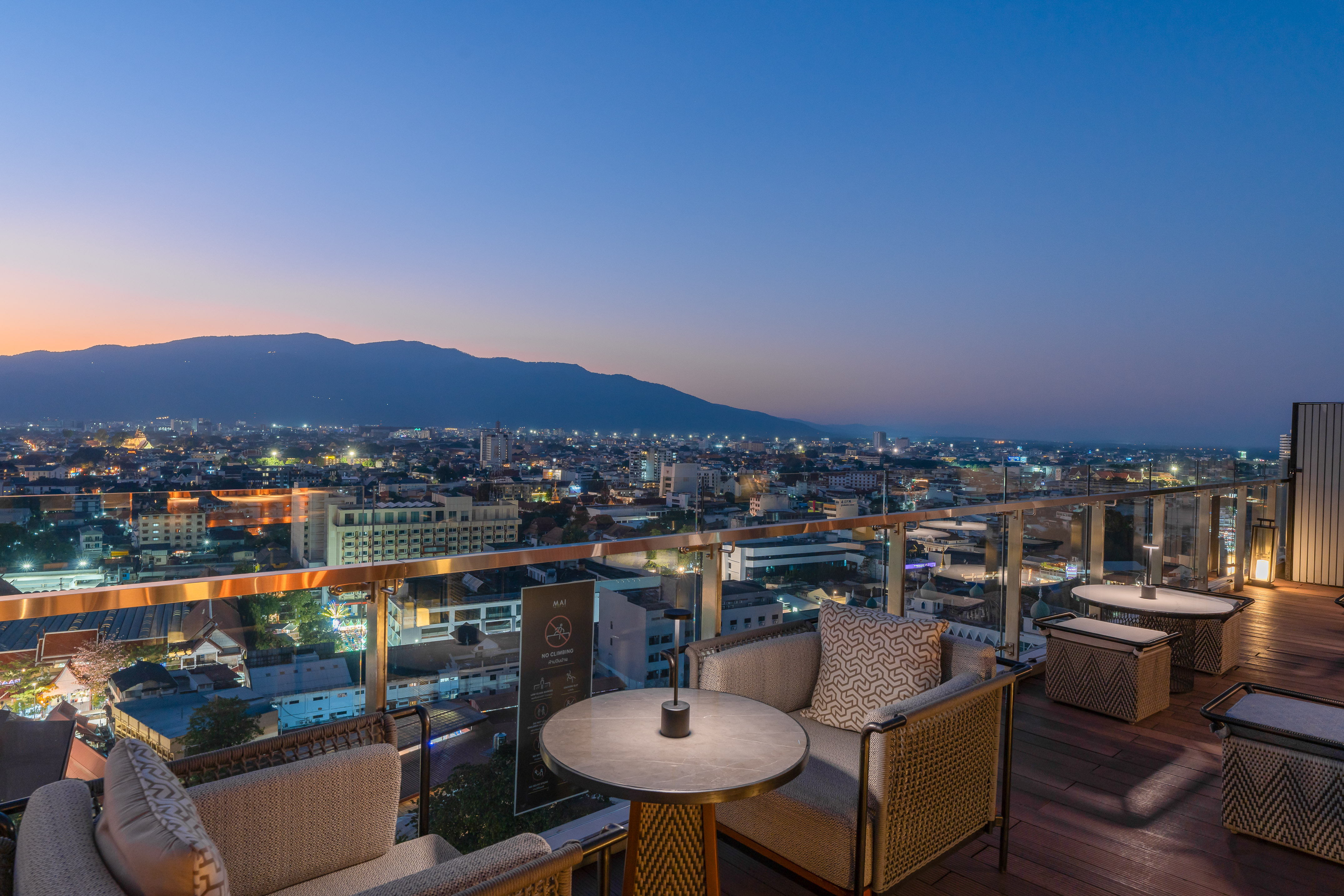 Rooftop bar overlooking illuminated city skyline and mountains at dusk.