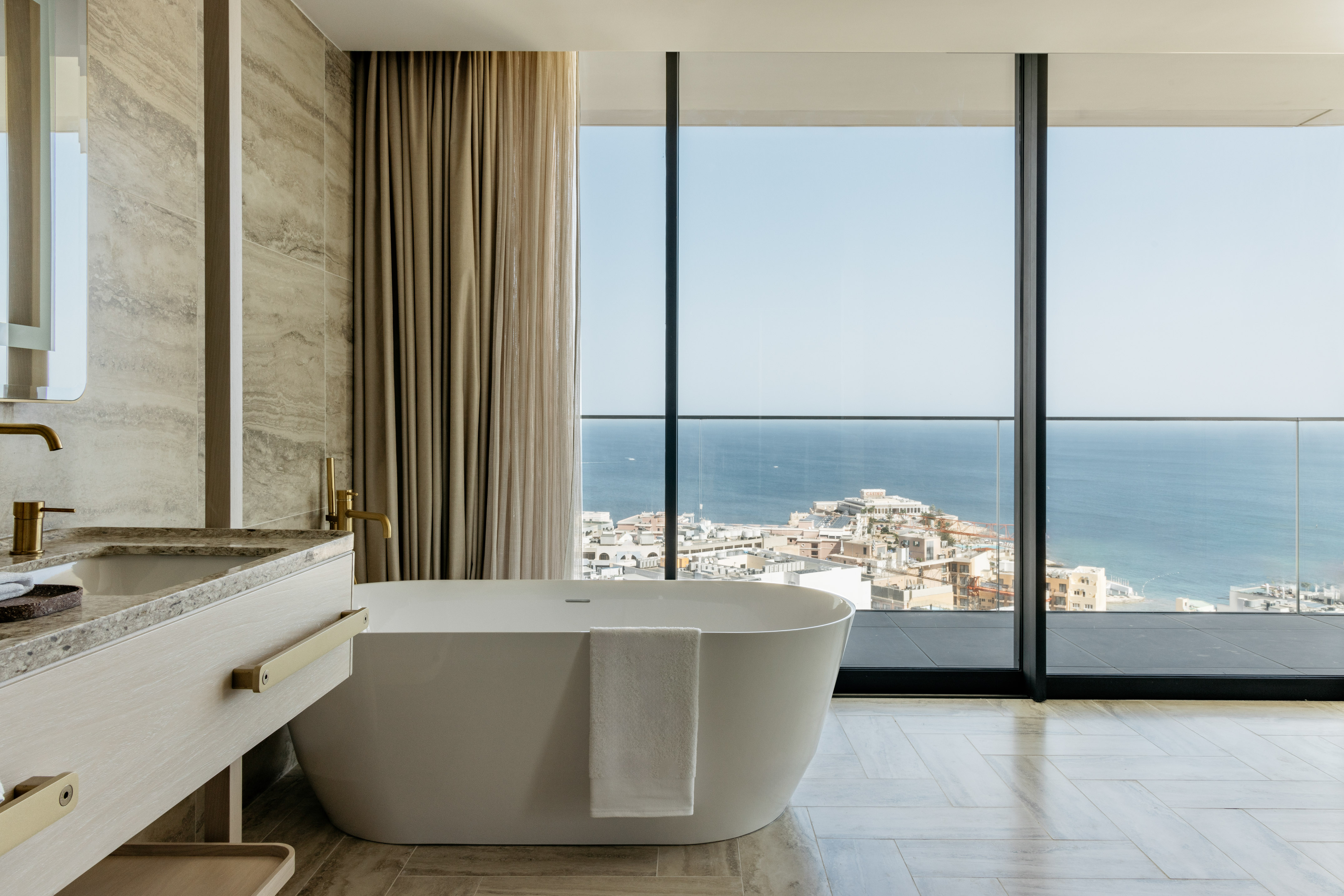 Modern luxury bathroom with freestanding tub and stunning ocean city view.