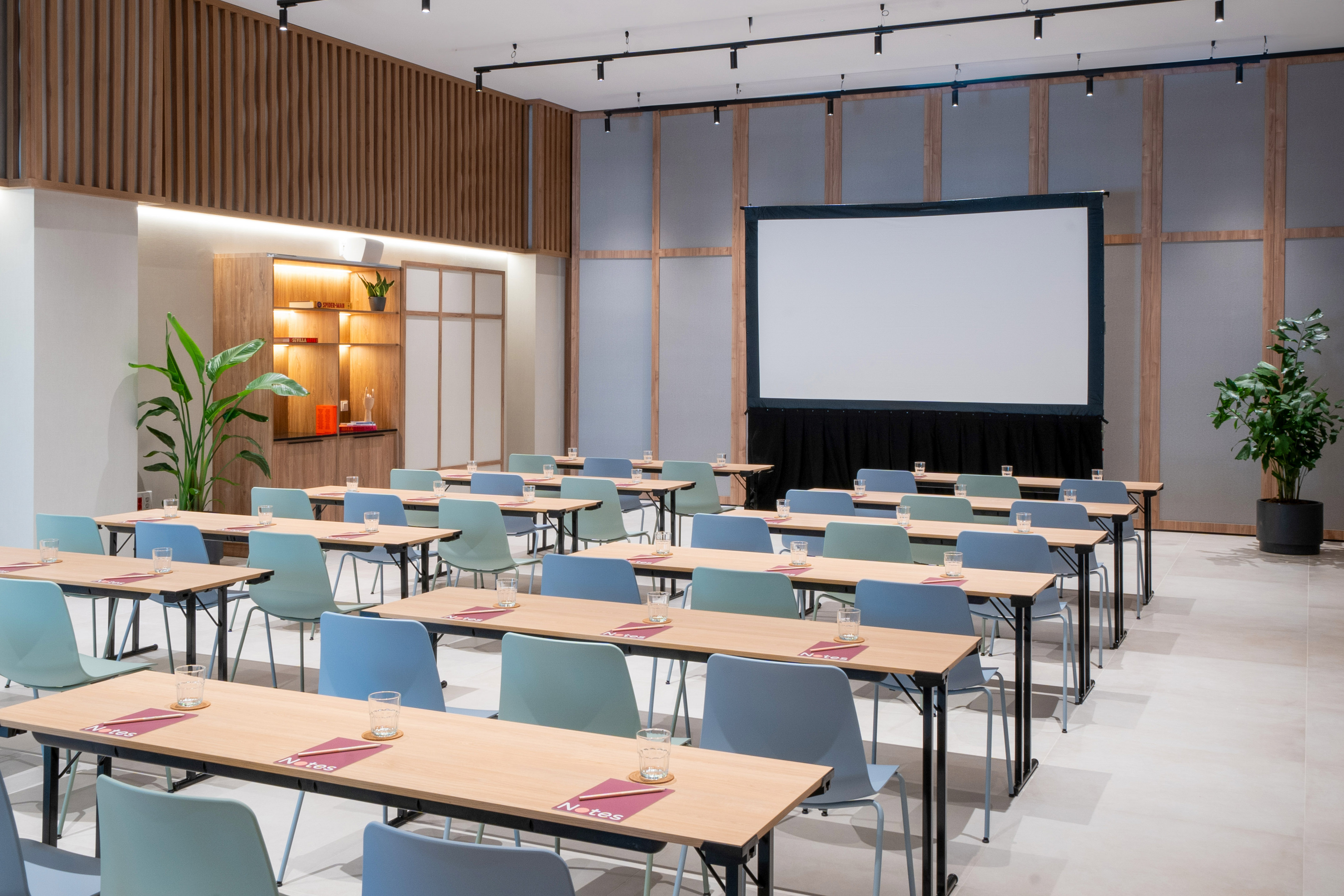 Modern conference room with tables, blue chairs, and a large presentation screen.