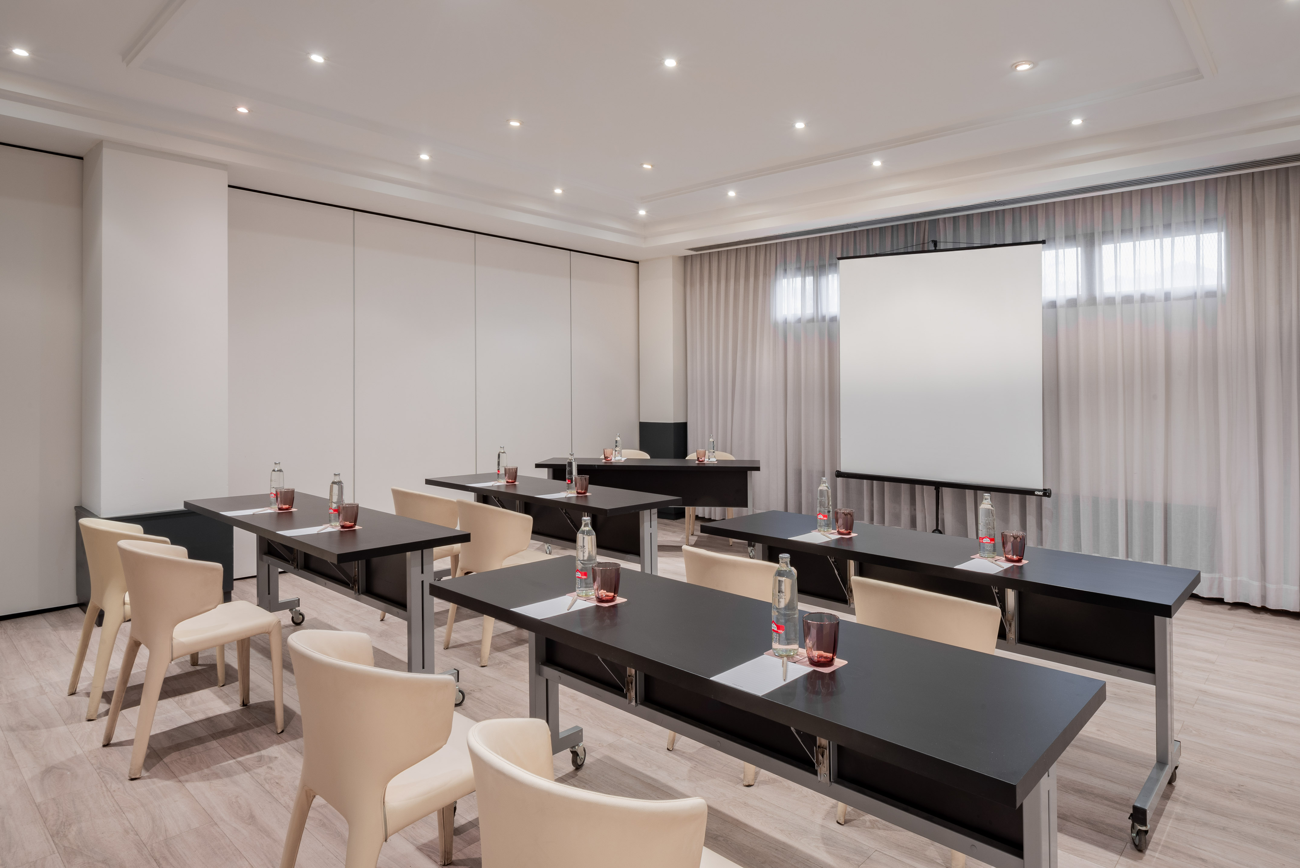 Modern meeting room with classroom setup, dark tables, light chairs, and projector screen.