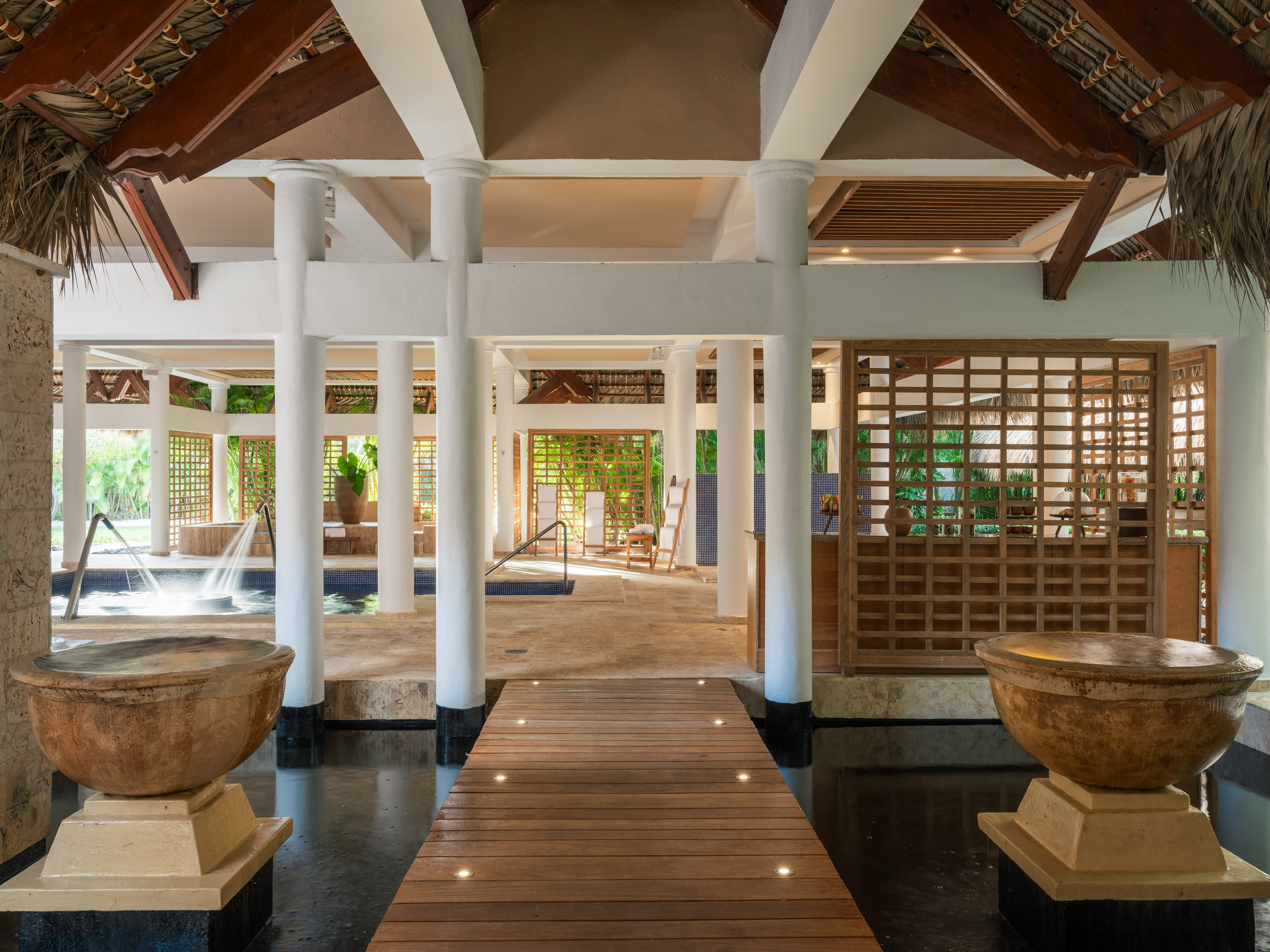 Tropical resort spa with wooden walkway, water features, stone bowls, and columns.