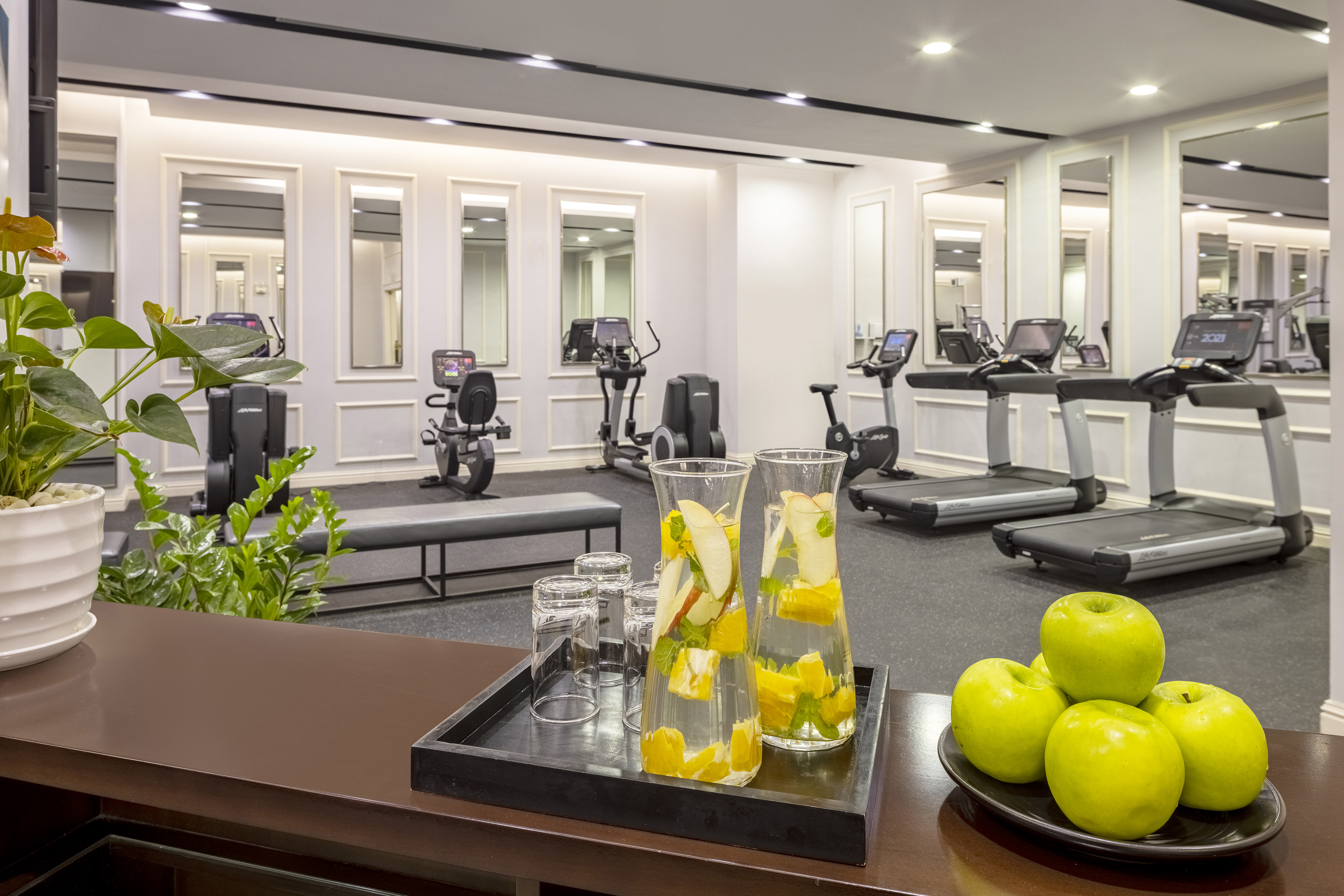 Hotel gym with exercise equipment, infused water, and fresh green apples.