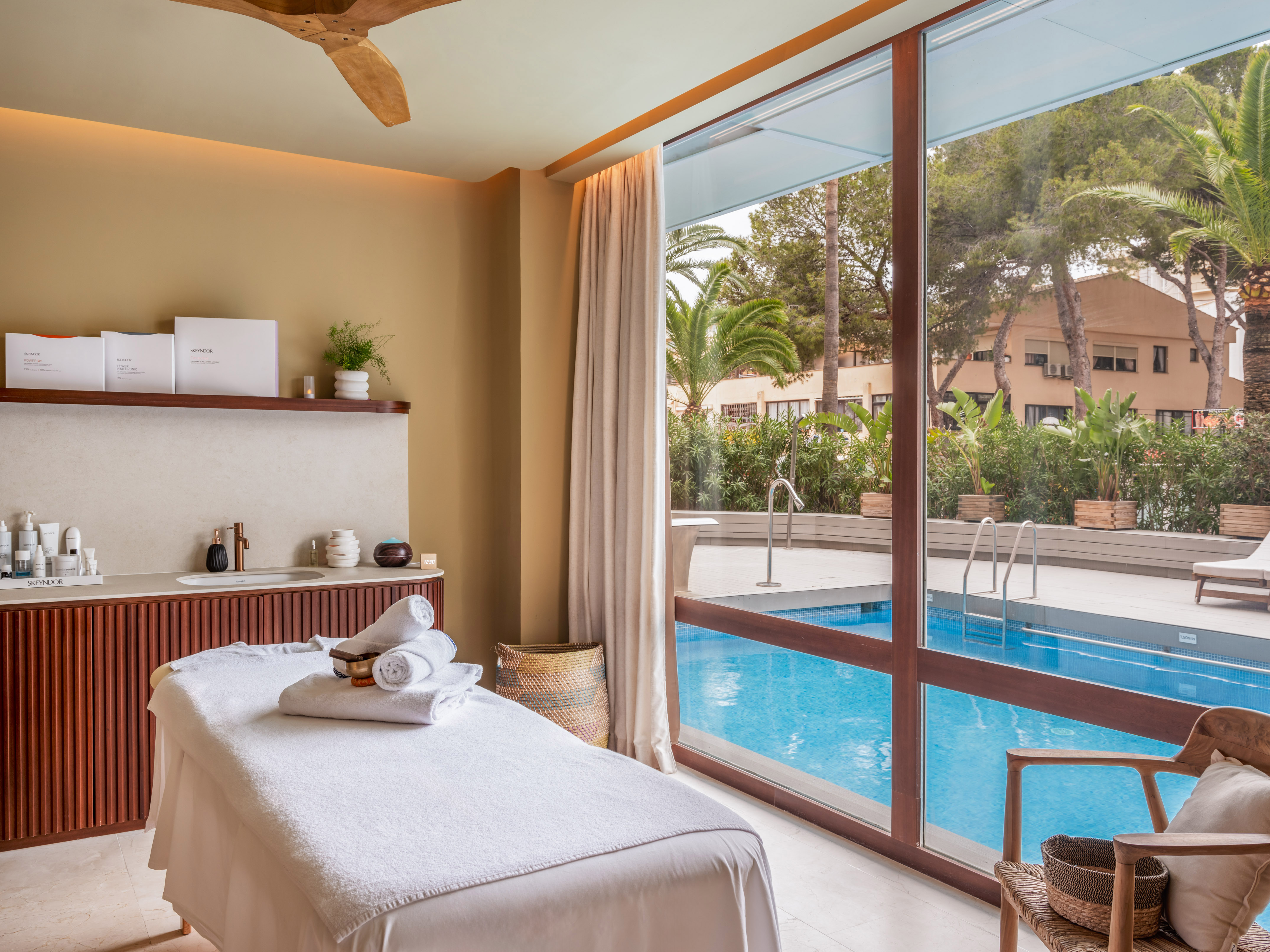 Tranquil spa treatment room with massage bed, pool view, and Skeyndor products.