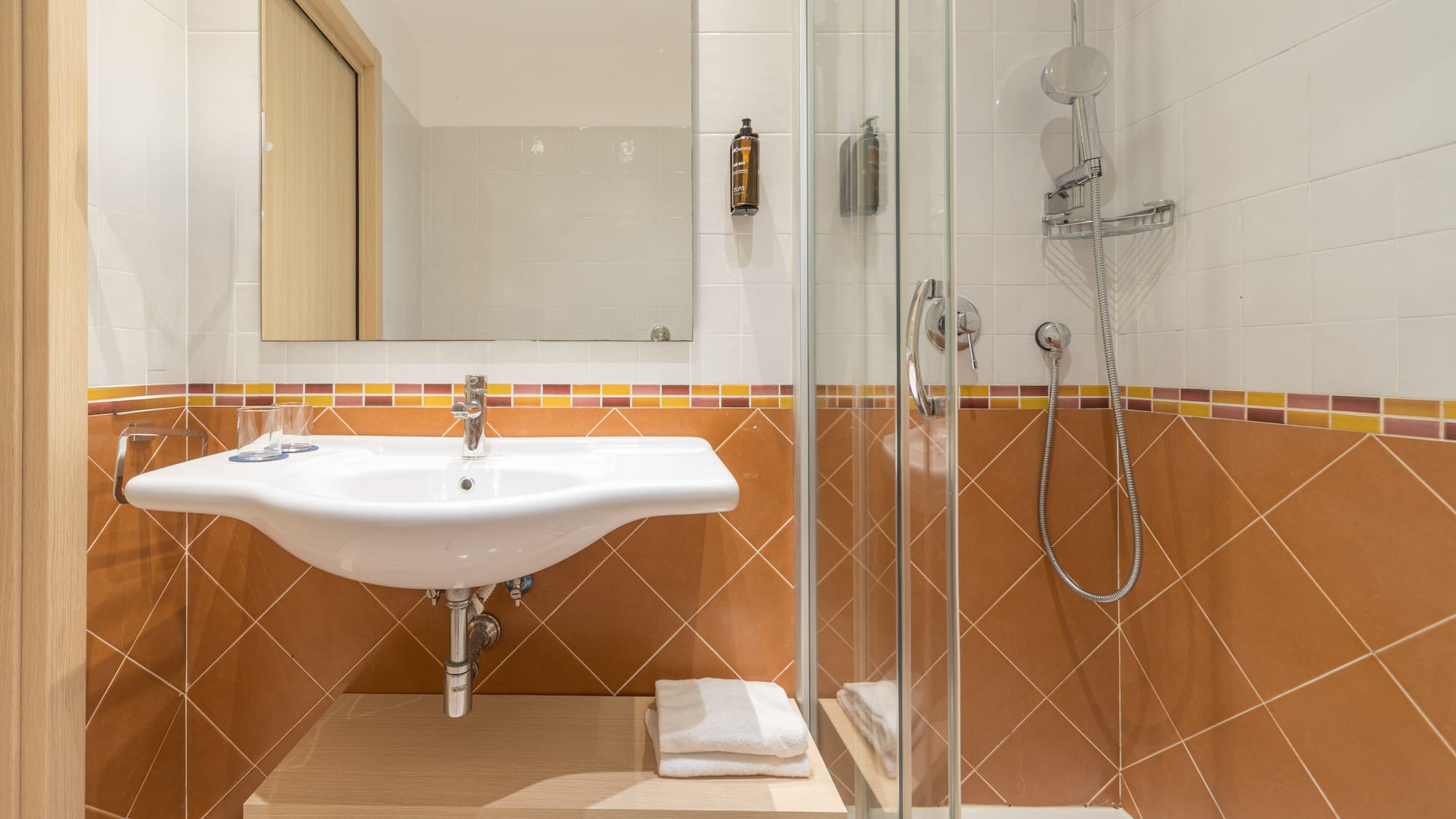 Hotel bathroom with white sink, mirror, glass shower, brown and white tiles.
