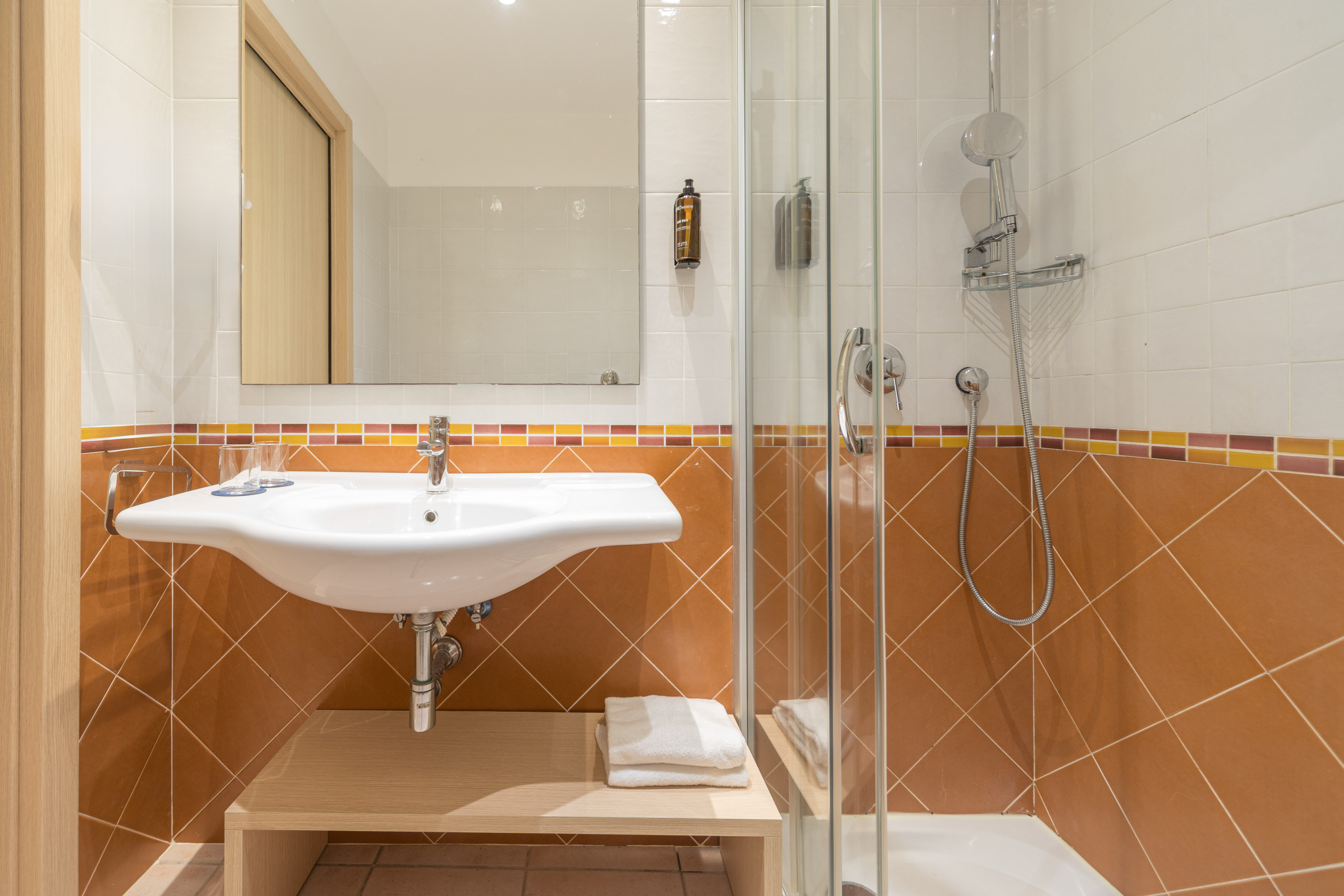 Hotel bathroom with white sink, mirror, glass shower, brown and white tiles.