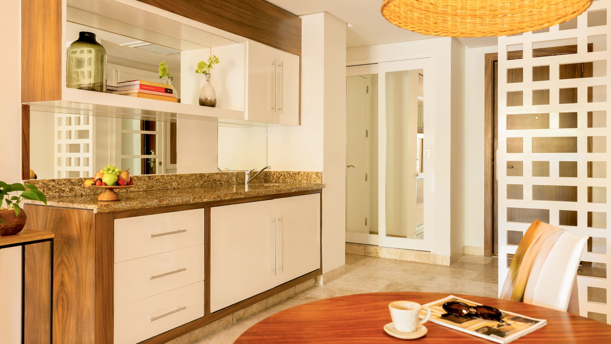 Contemporary hotel kitchenette with granite counter, mirror, and dining table.