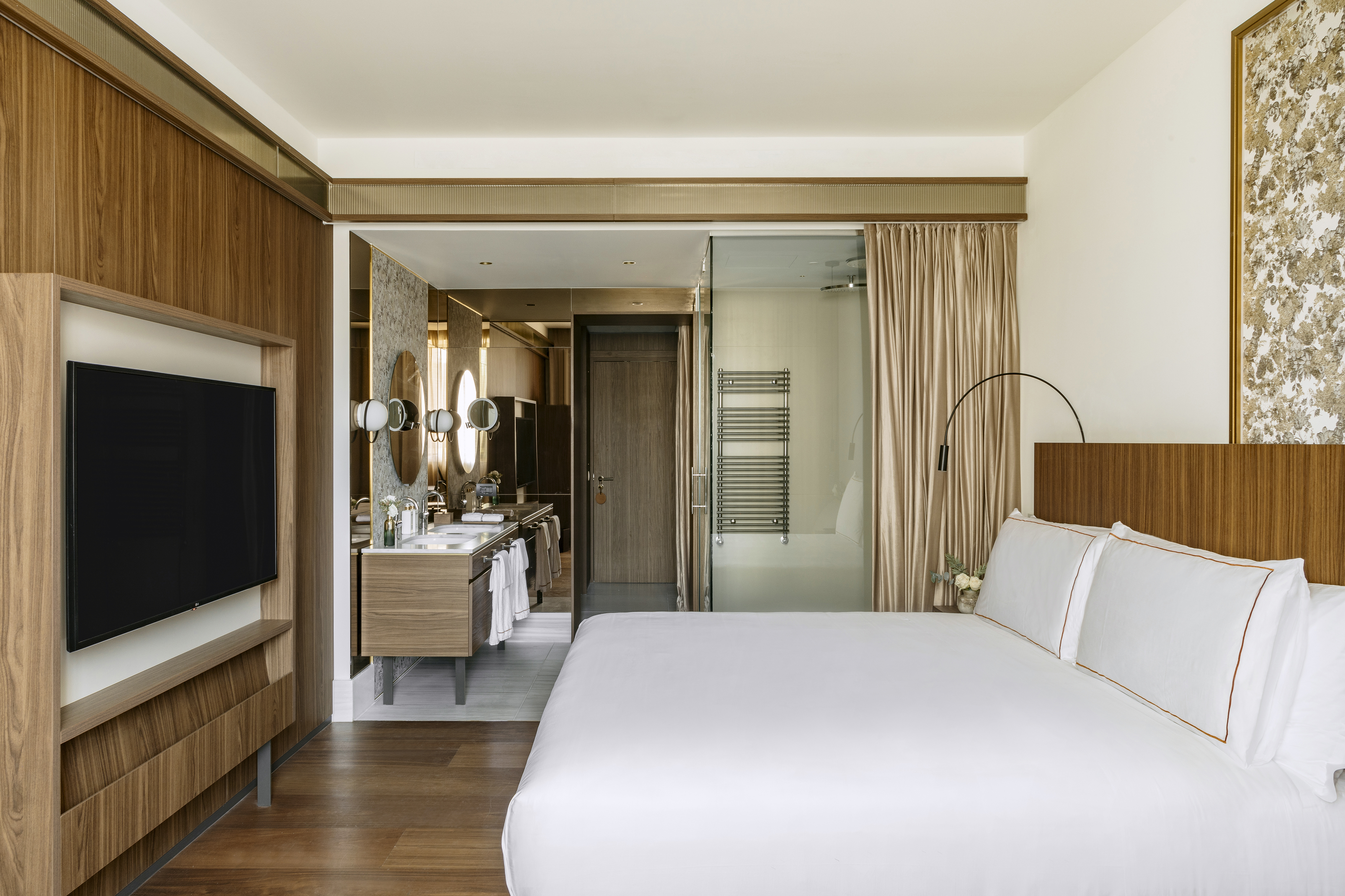 Modern hotel room with king bed, wood paneling, TV, and open bathroom.