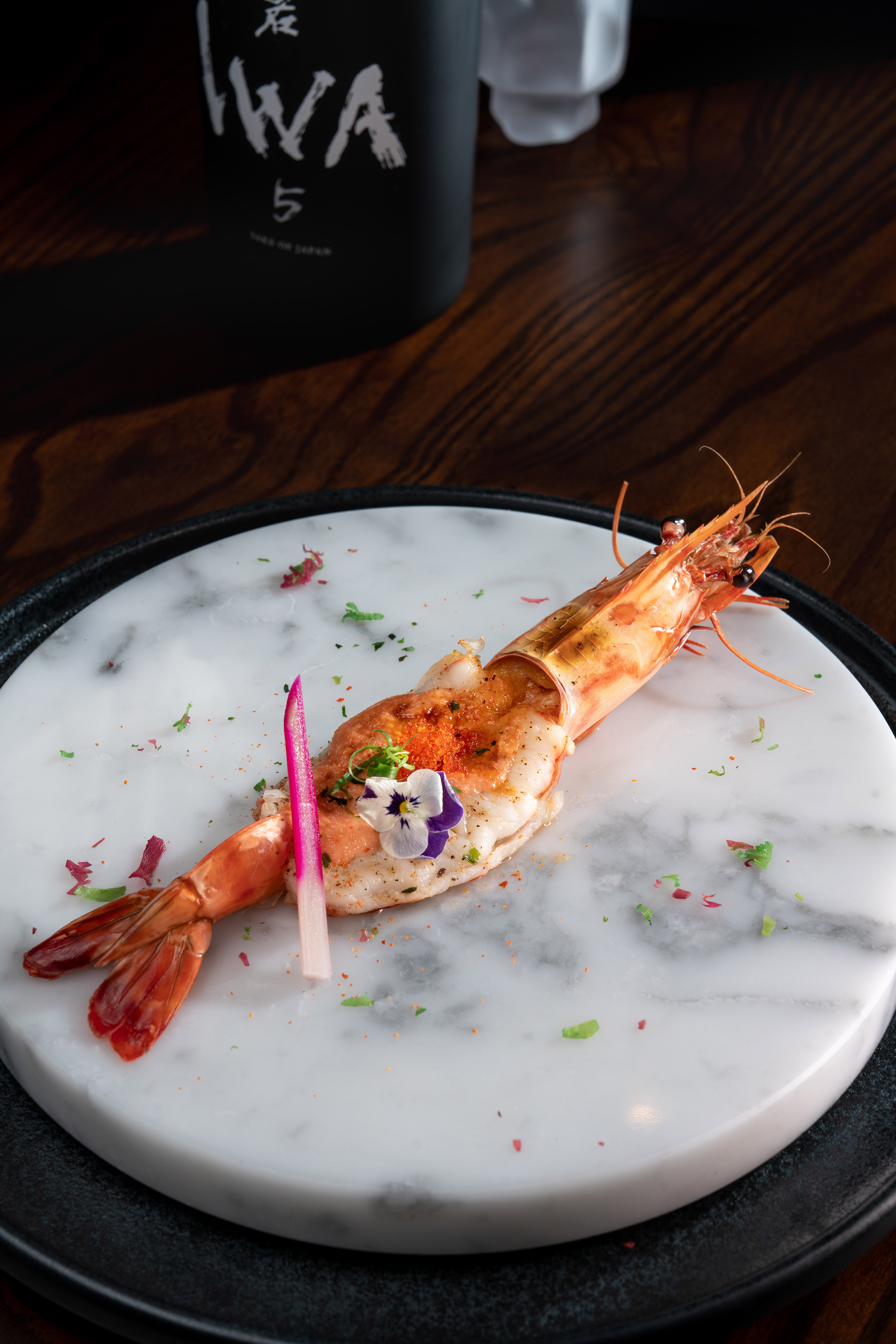 Gourmet Japanese prawn with tobiko and edible flower on marble plate.