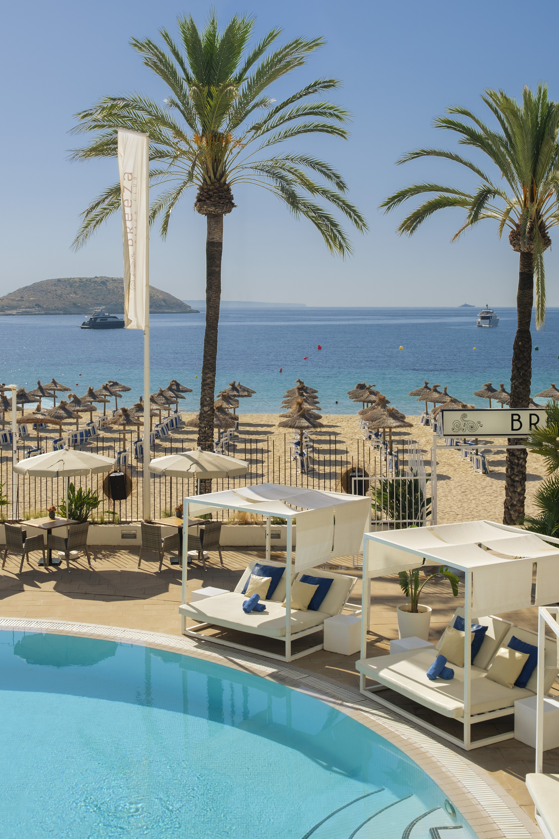Tropical resort pool and beach with cabanas, palm trees, and blue ocean.