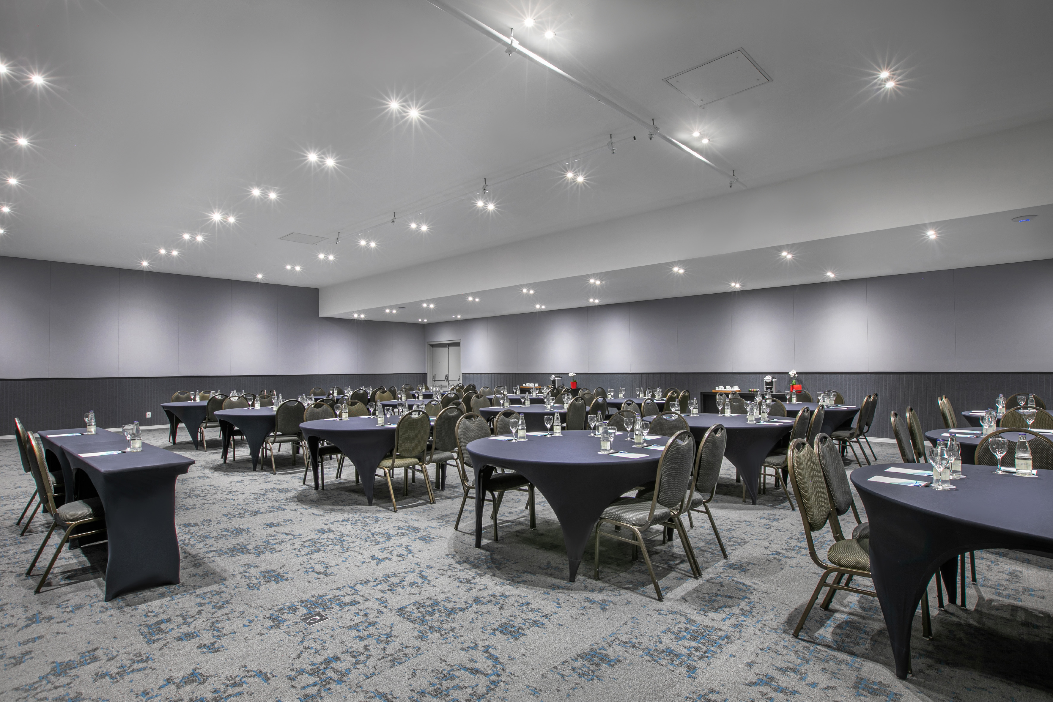 Empty event space with round tables, chairs, and bright ceiling spotlights.