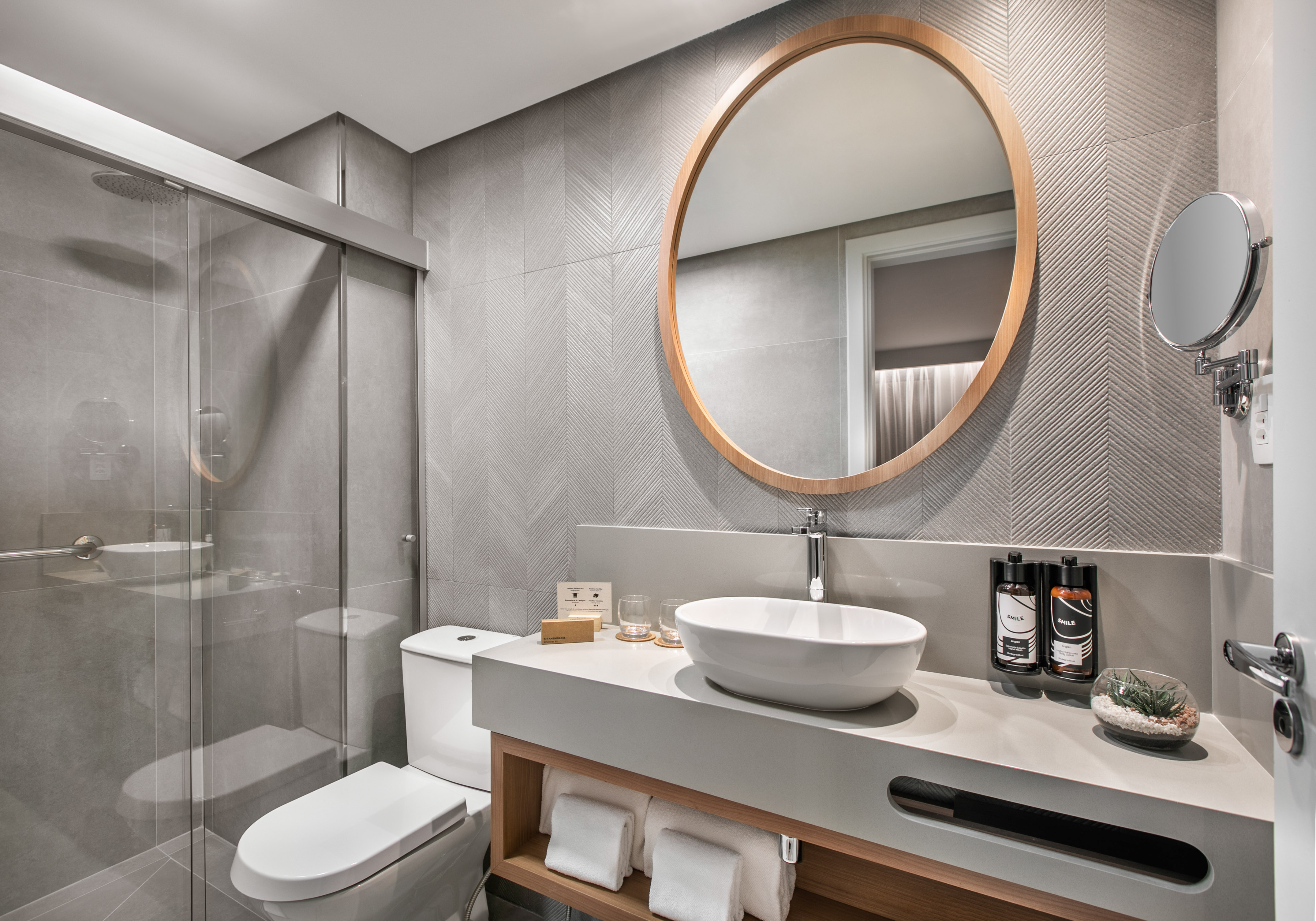 Modern gray tiled bathroom with round mirror, vessel sink, and glass shower.
