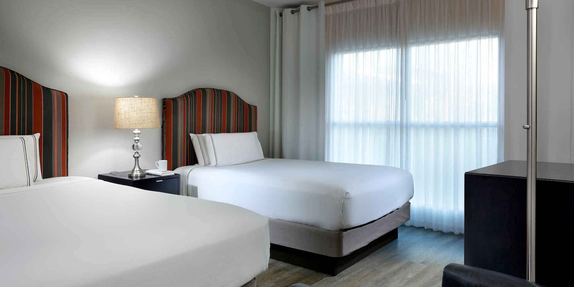 Hotel room with two beds, striped headboards, and sheer window curtains.