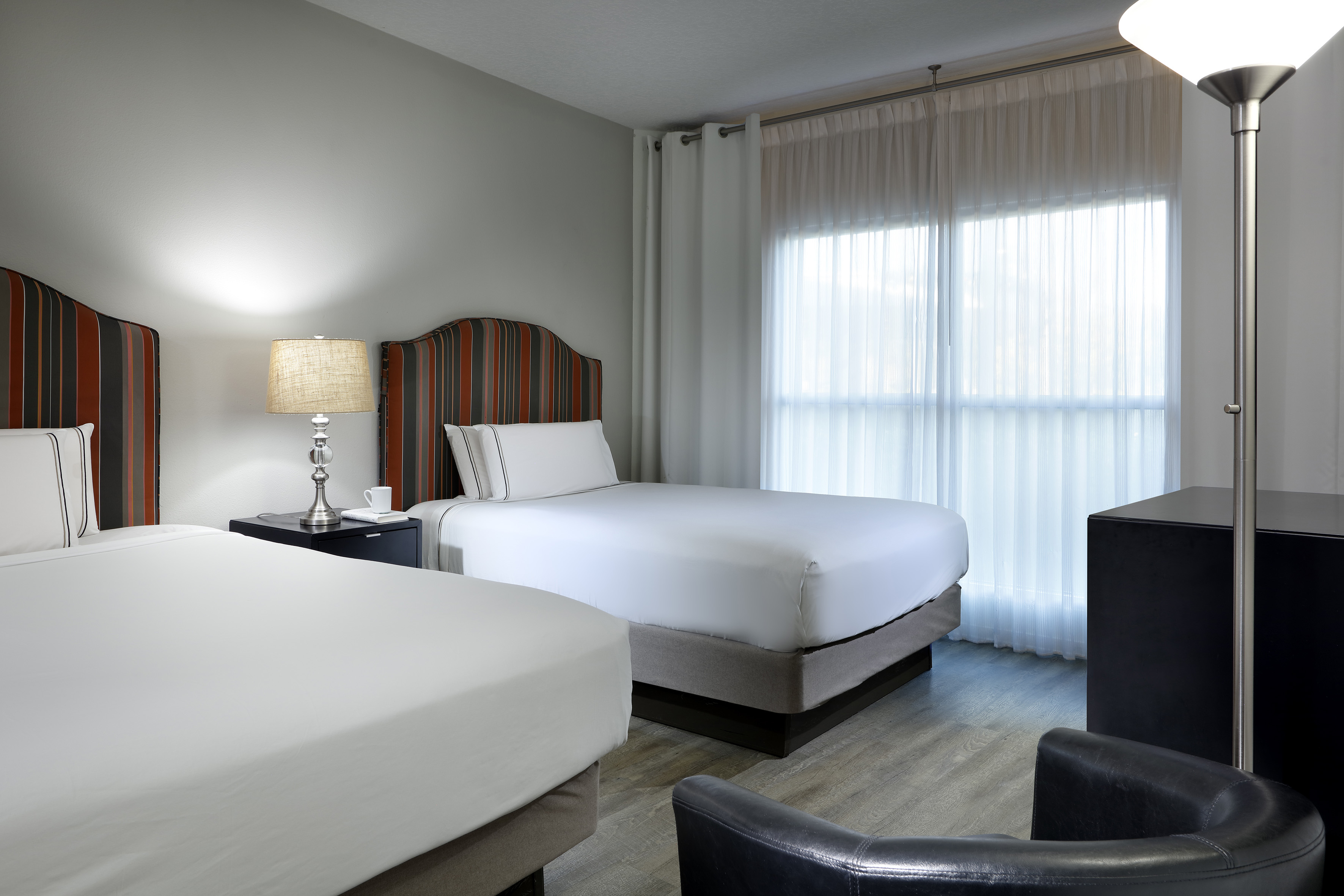 Hotel room with two beds, striped headboards, and sheer window curtains.