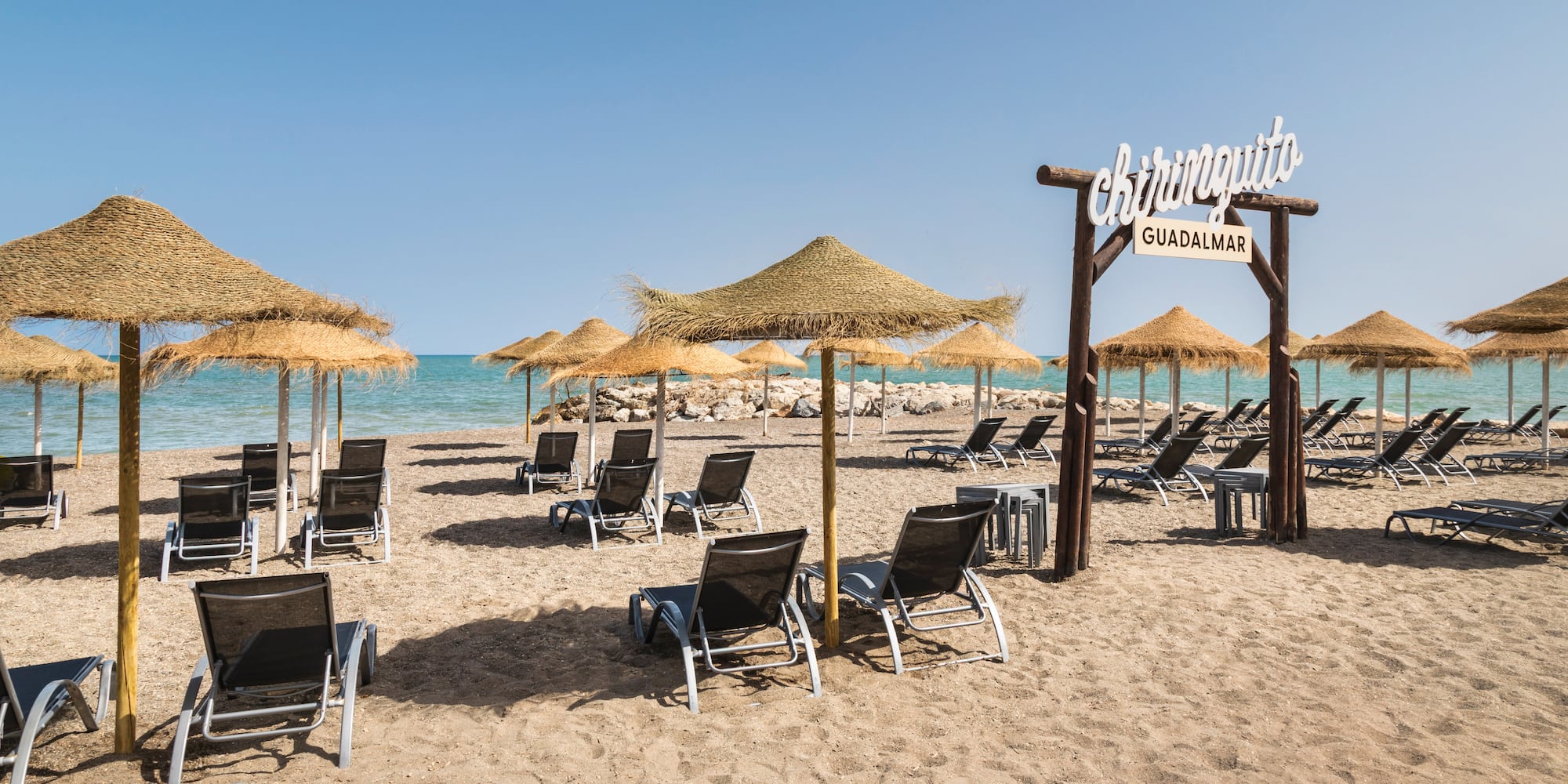 Chiringuito Guadalmar beach with straw umbrellas, sun loungers, and ocean.