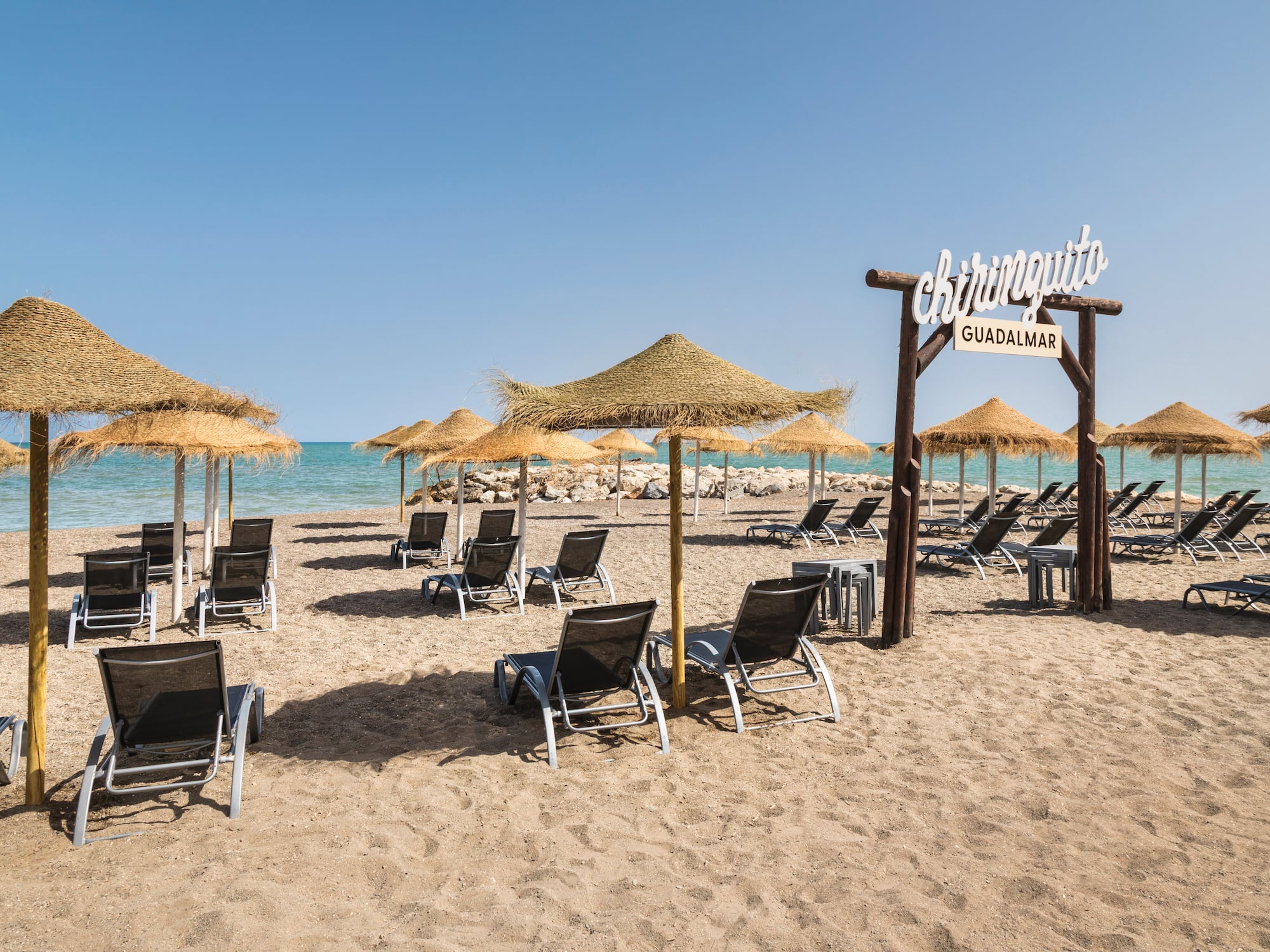 Chiringuito Guadalmar beach with straw umbrellas, loungers, and ocean.