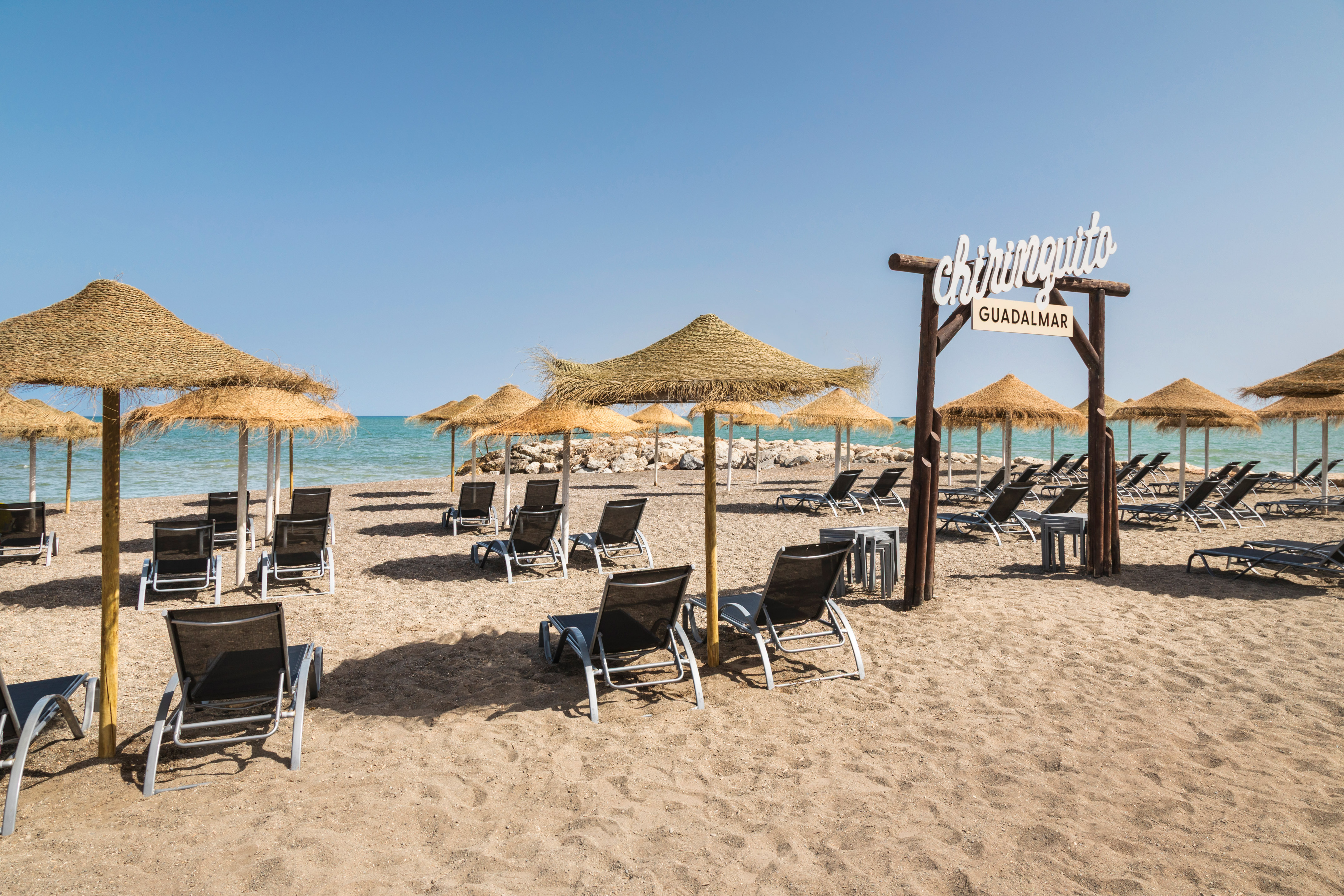 Chiringuito Guadalmar beach with straw umbrellas, sun loungers, and ocean.