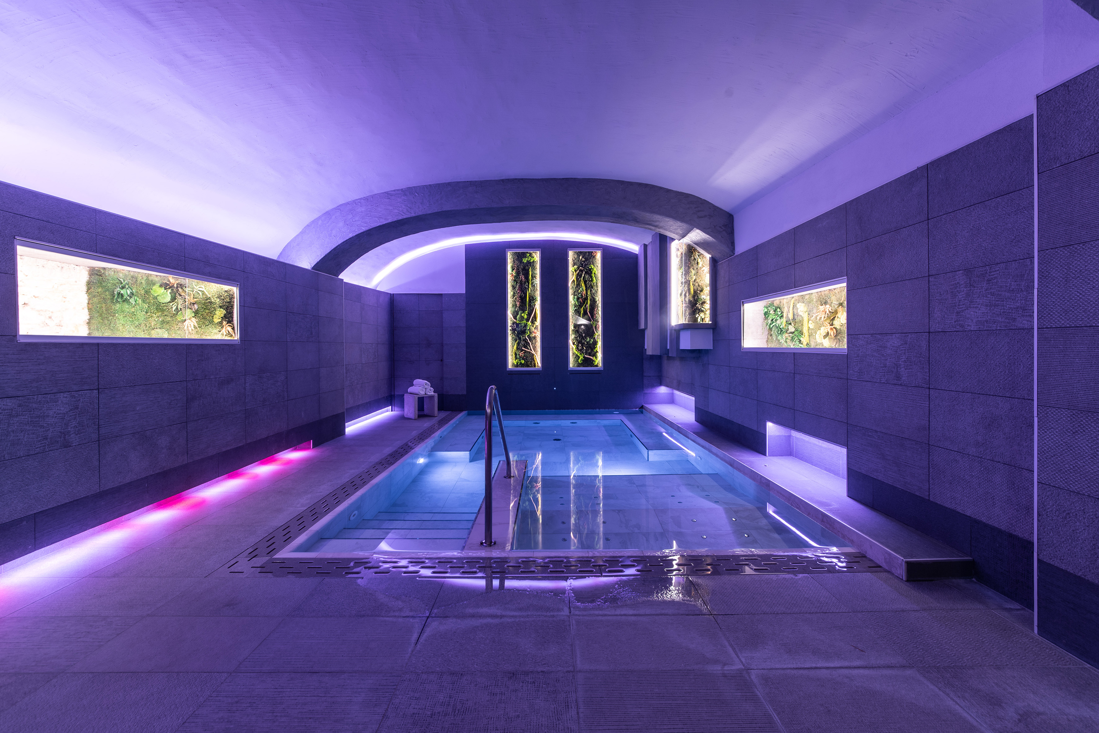 Modern indoor spa pool with purple lighting and green living walls.