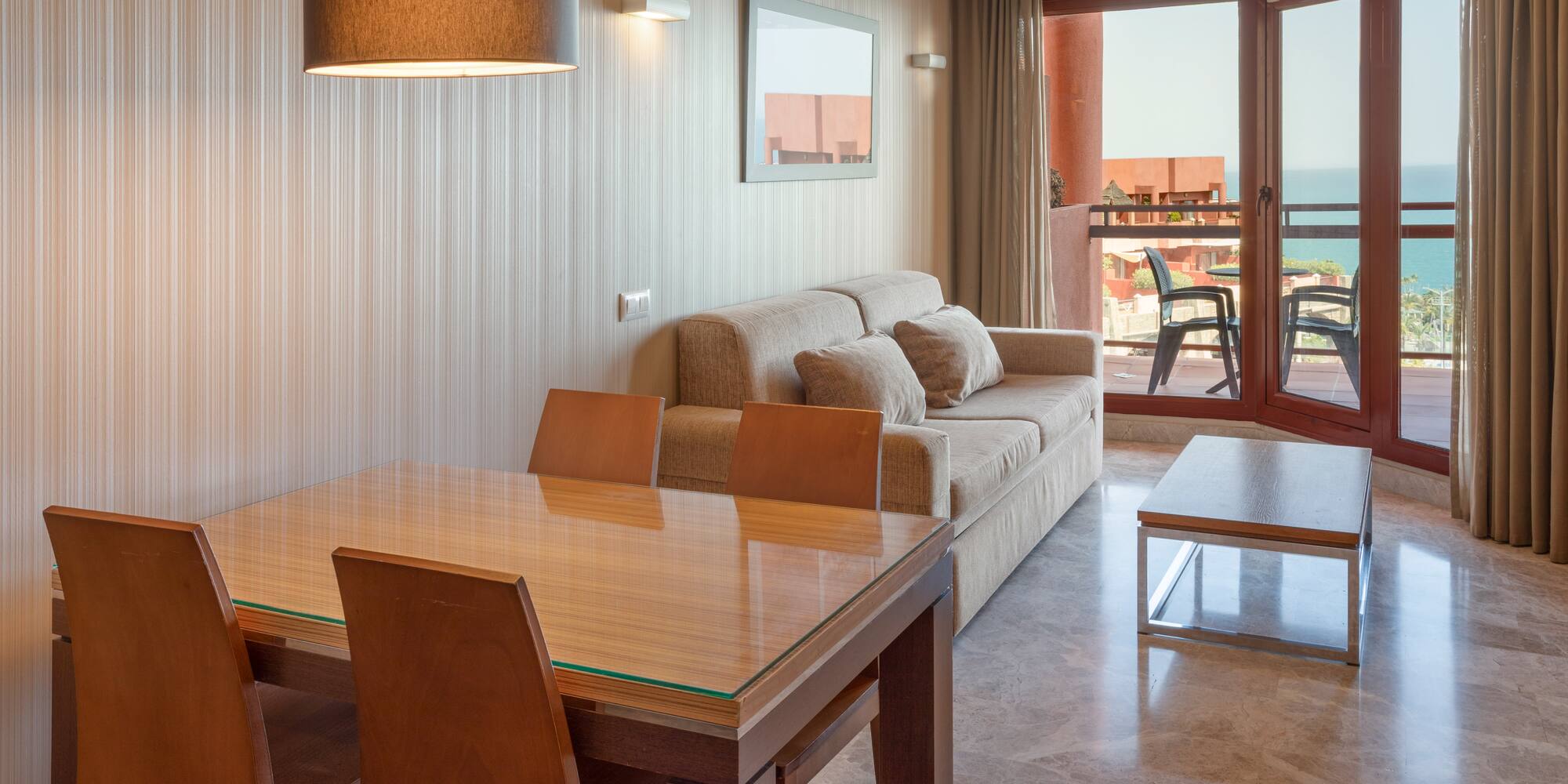 Apartment living room with dining table, sofa, and ocean view balcony.