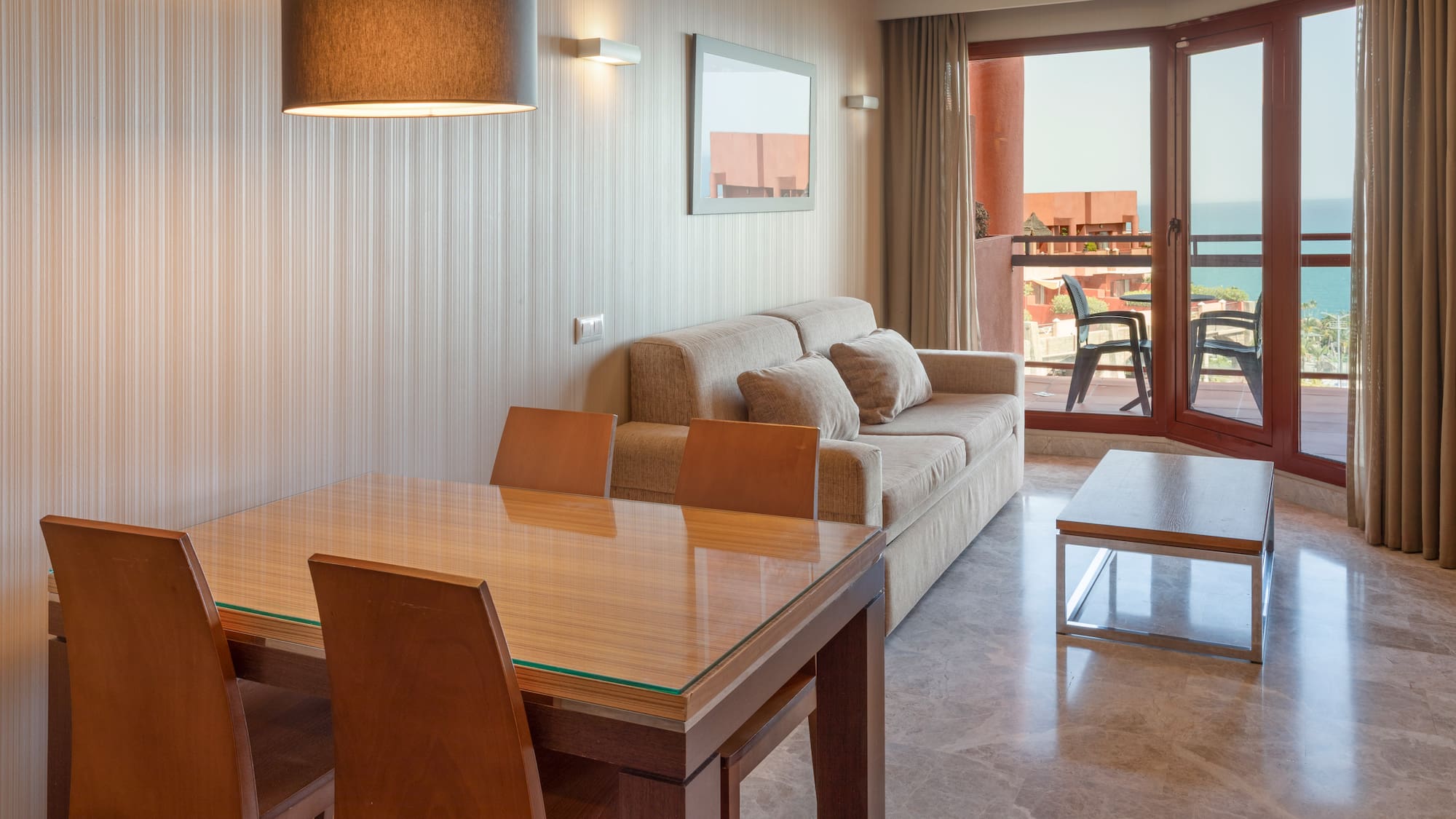 Apartment living room with dining table, sofa, and ocean view balcony.