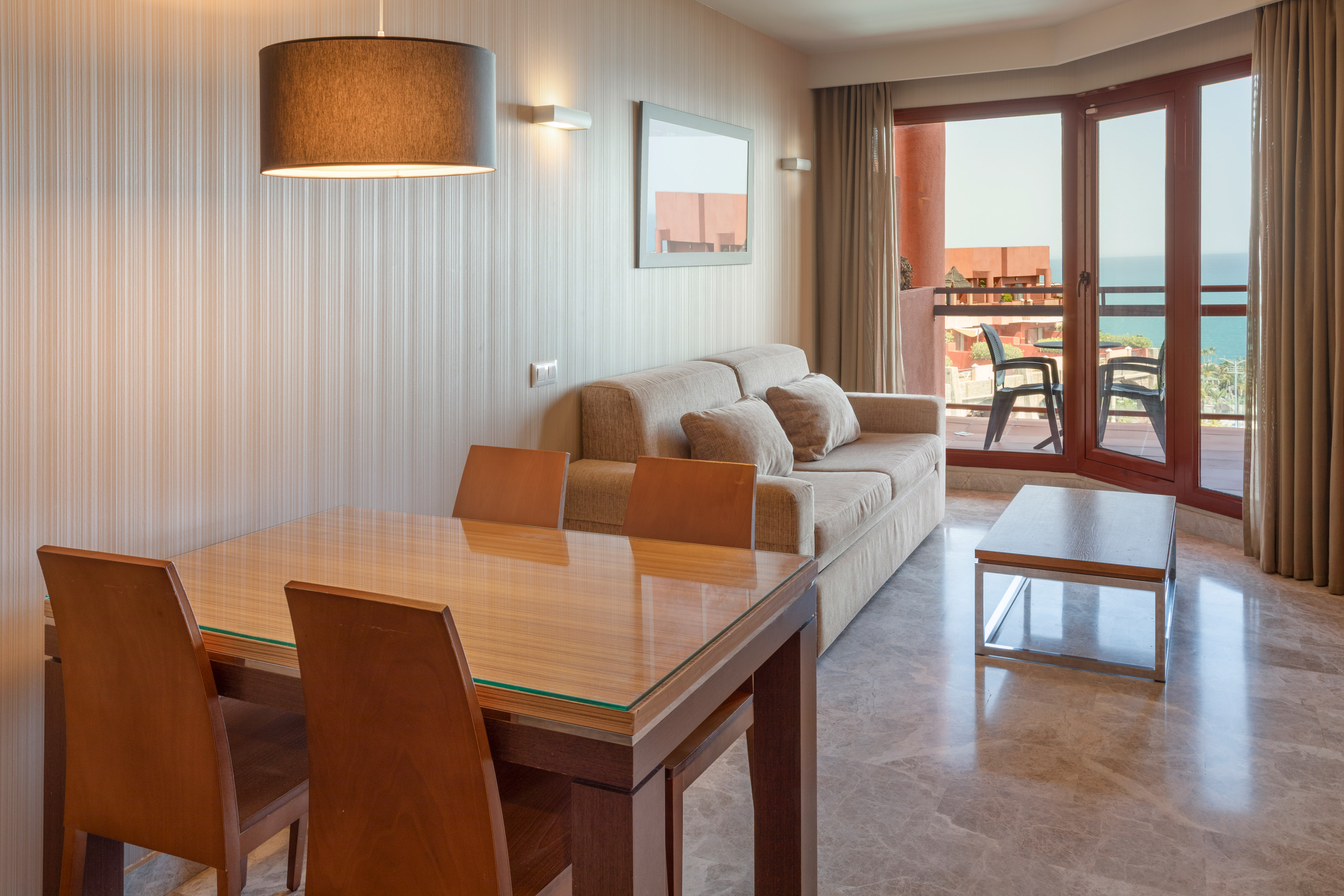 Modern apartment living room with dining table, sofa, and ocean view balcony.