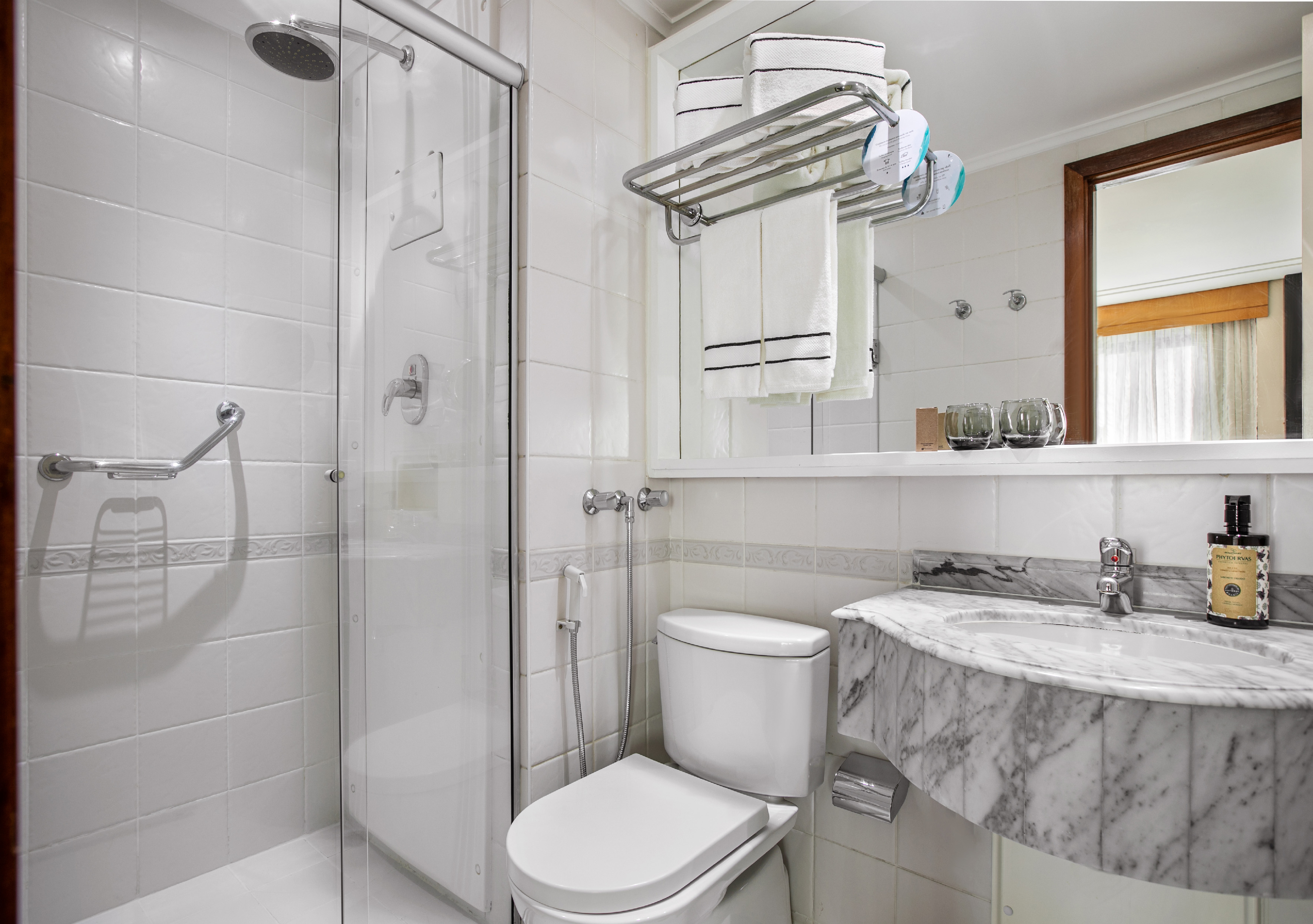 Modern hotel bathroom with white tiles, glass shower, toilet, and marble sink.