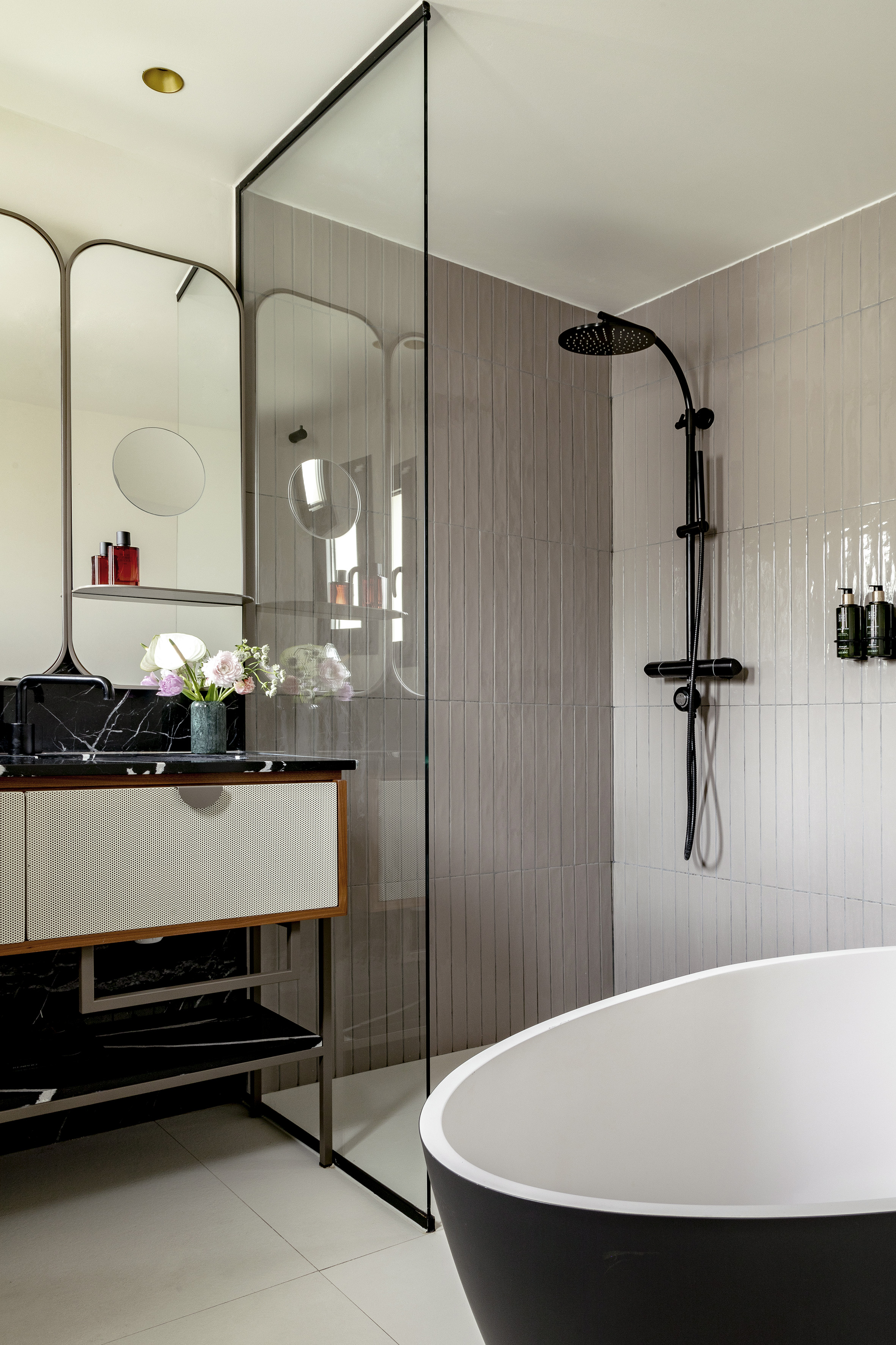 Modern luxury bathroom with black tub, glass shower, vanity, and grey tiles.