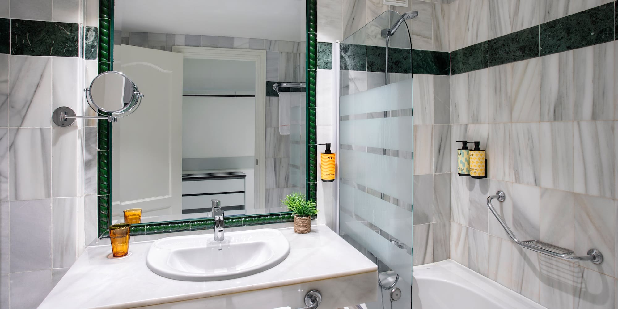 Marble hotel bathroom with vanity, sink, green accents, and shower-bathtub combo.