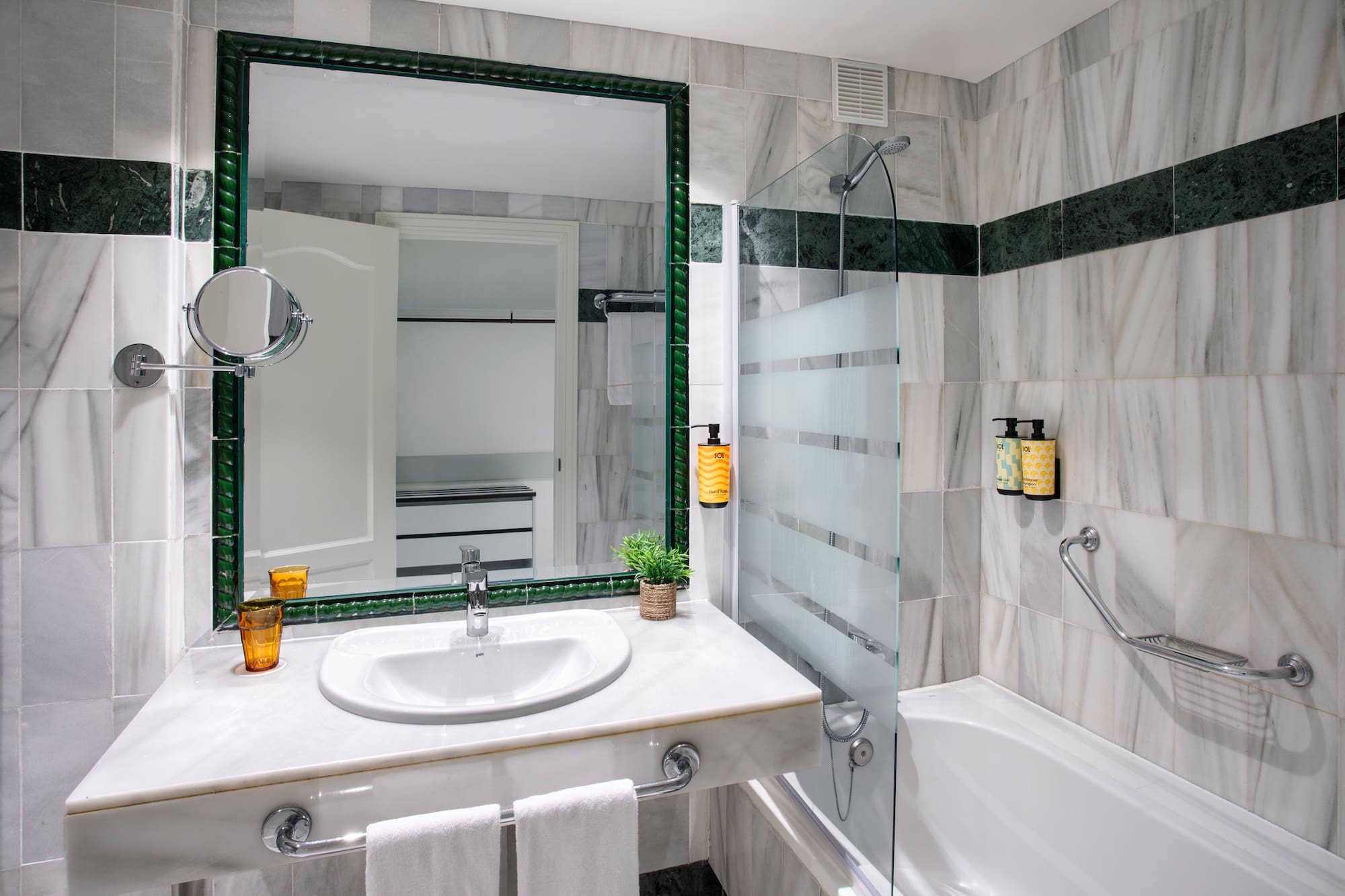 Baño elegante con paredes de mármol y detalles verdes, lavabo, espejo y ducha.