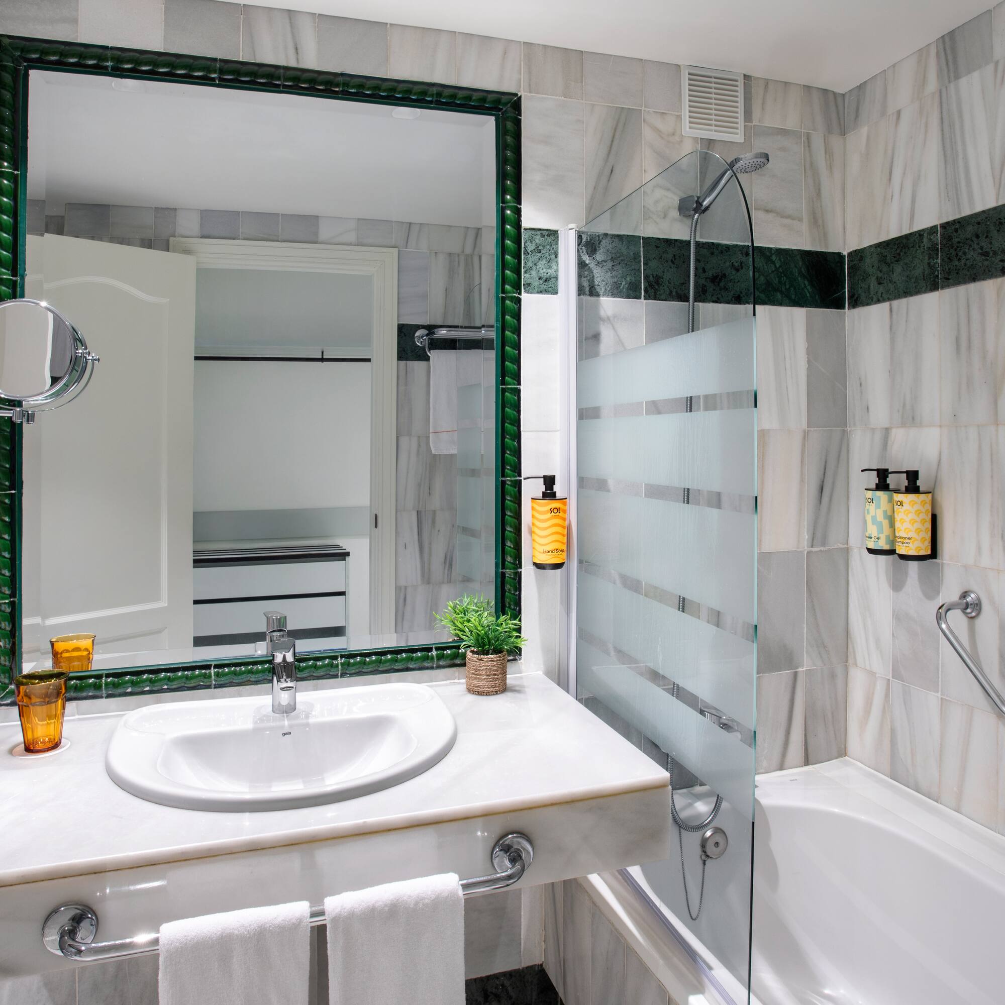 Baño elegante con paredes de mármol y detalles verdes, lavabo, espejo y ducha.