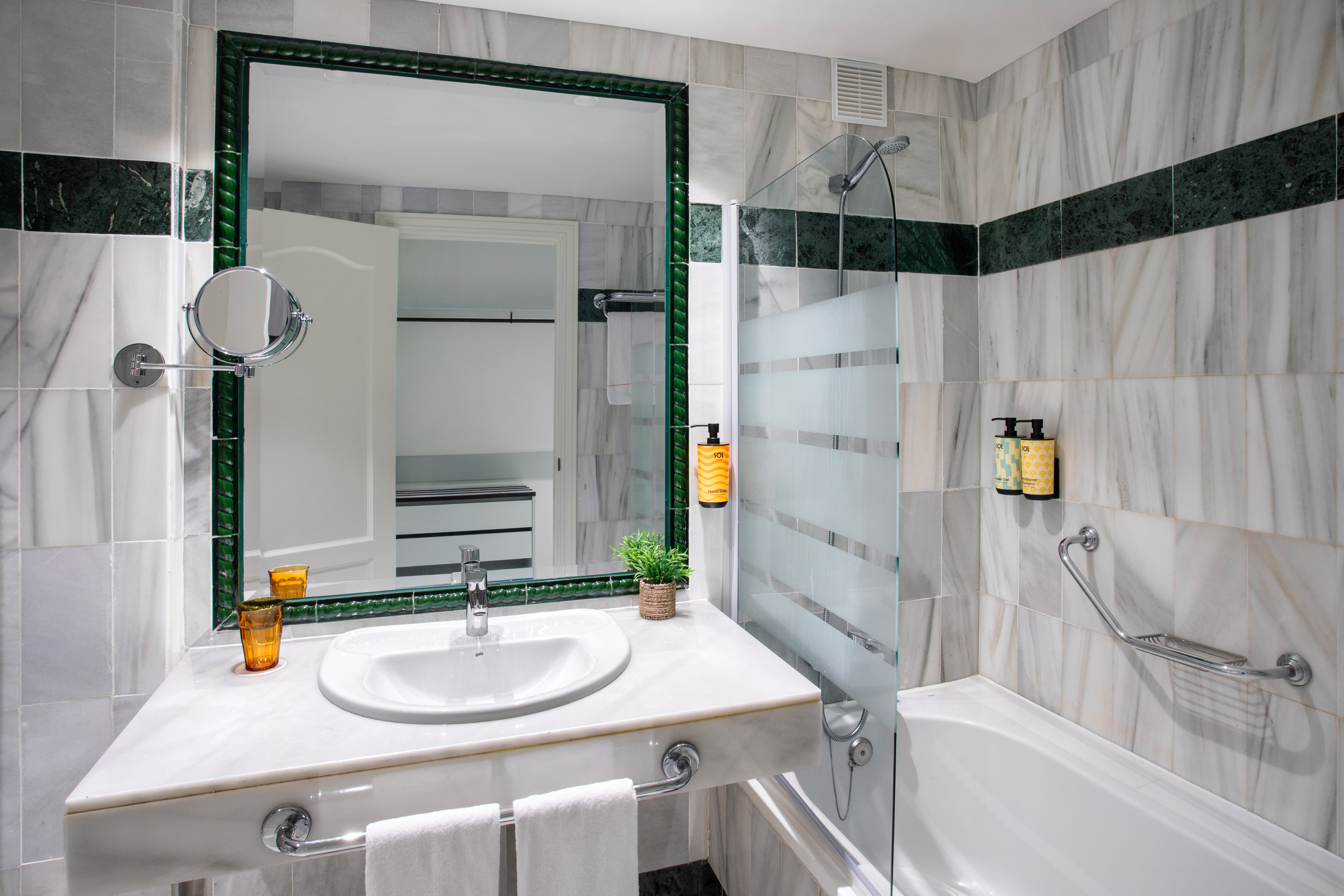 Marble hotel bathroom with vanity, sink, green accents, and shower-bathtub combo.