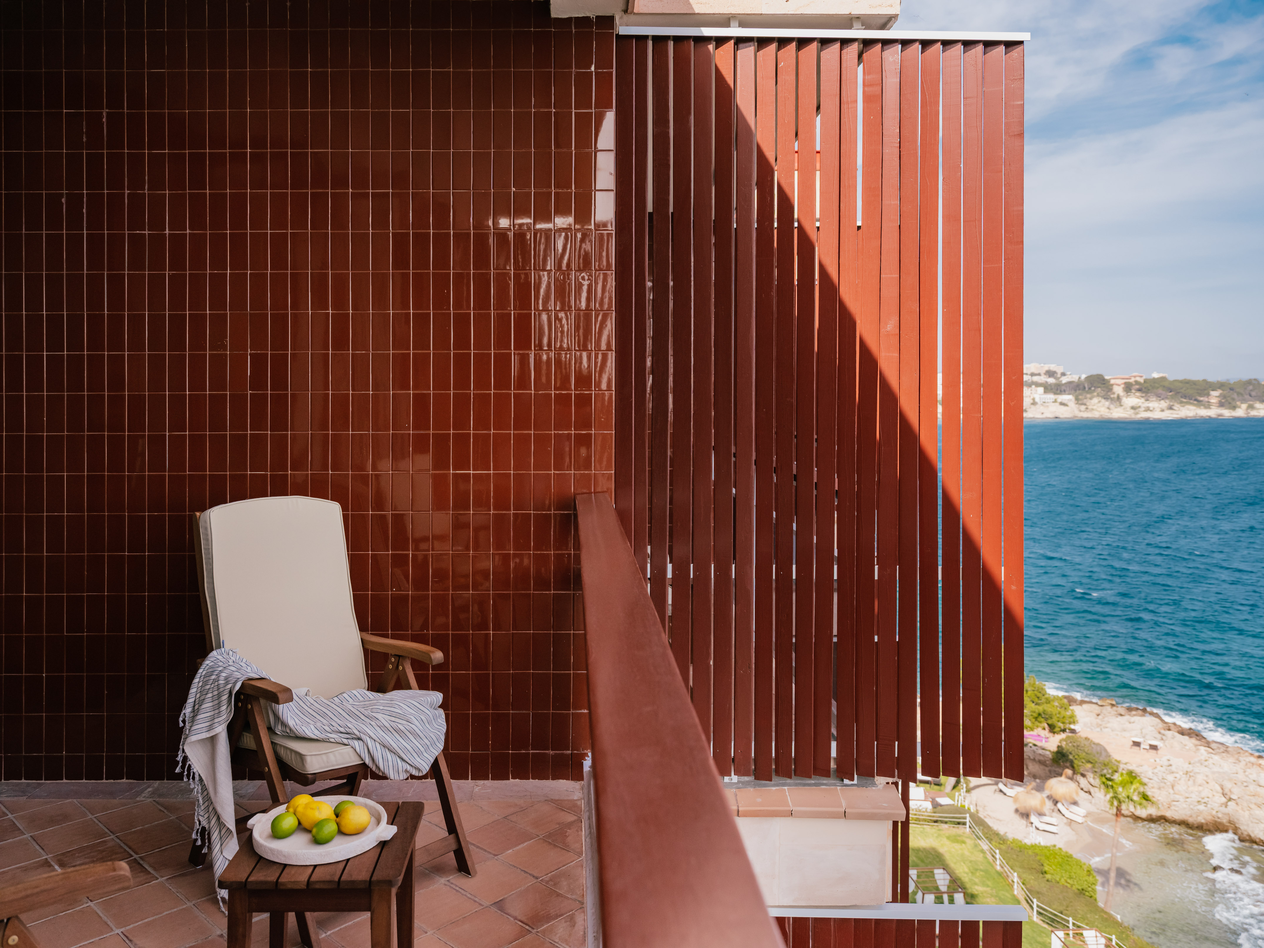 Sunny balcony overlooking sea, wooden chair, lemons, tiled wall & floor.