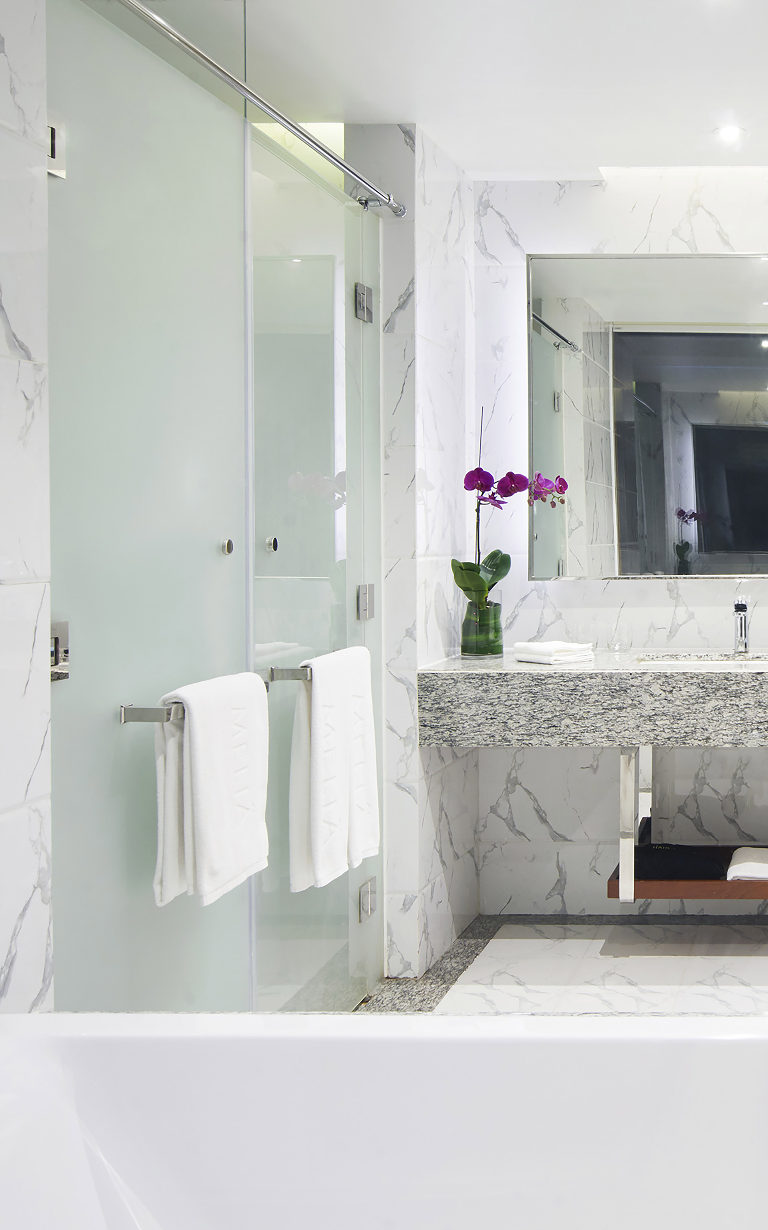 Modern marble bathroom with glass shower, vanity, and purple orchid.
