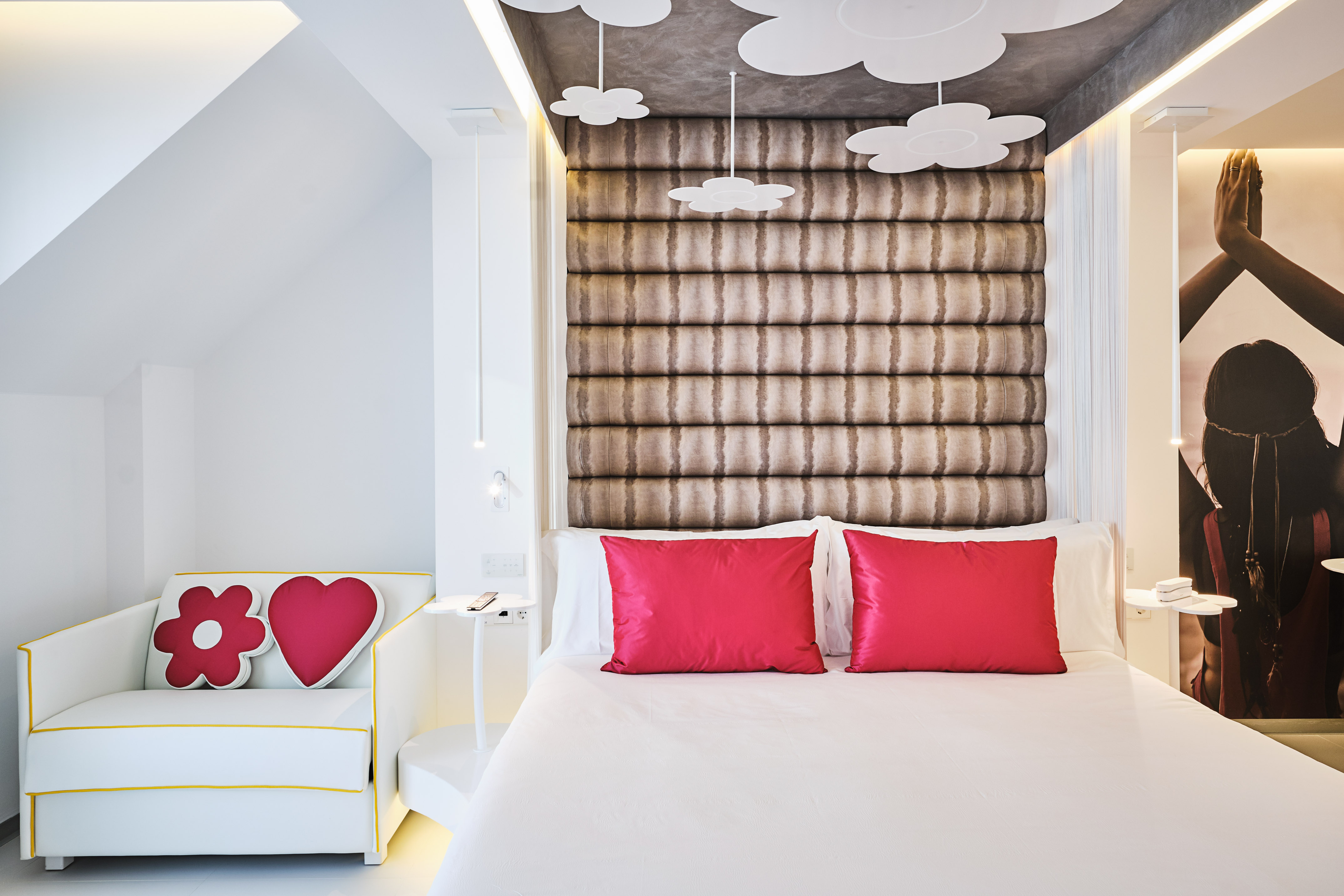 Modern hotel bedroom with white bed, red pillows, tufted headboard, cloud decor.