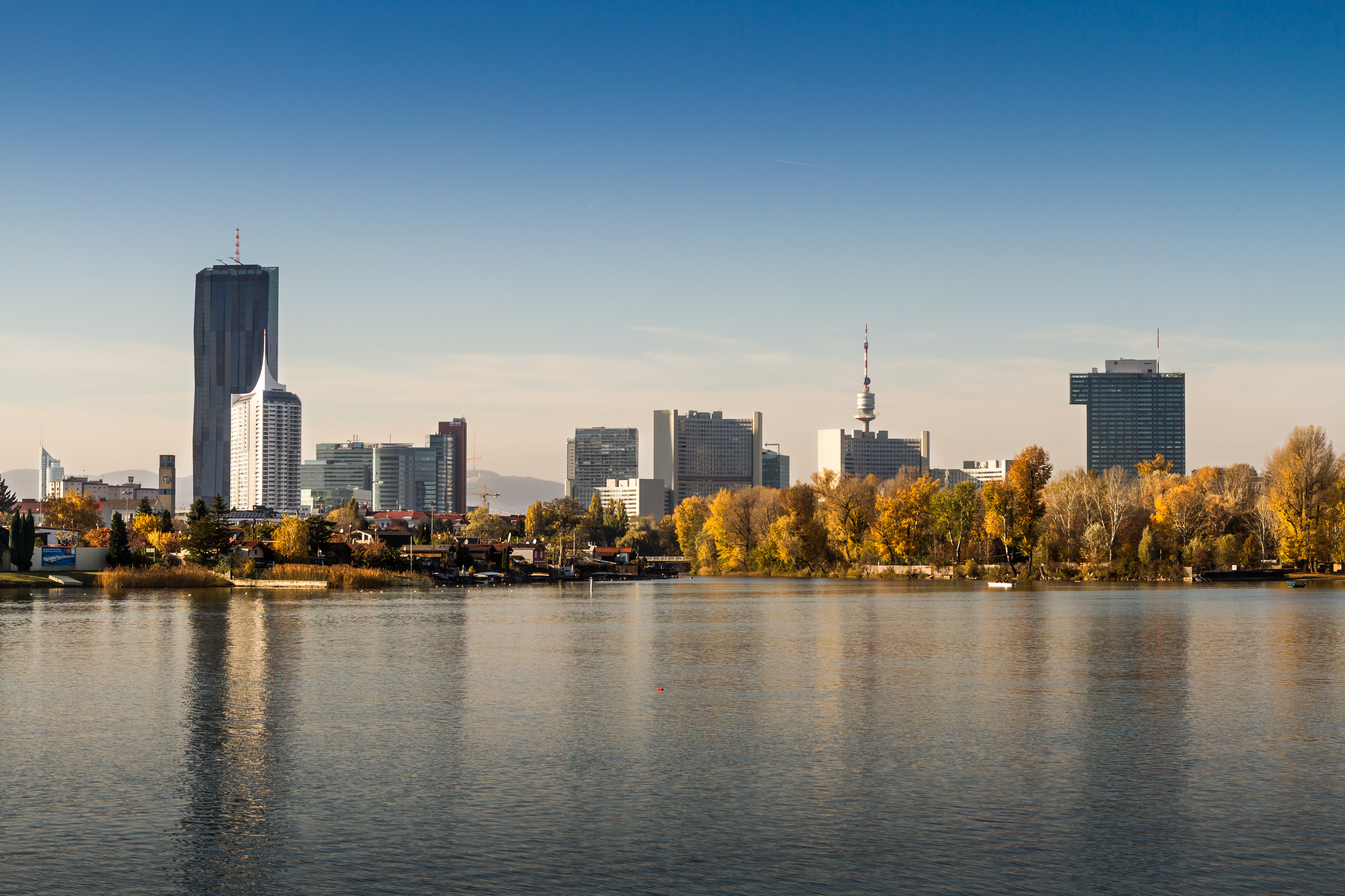 Vienna Donaucity skyline across Danube river with autumn trees and modern buildings.