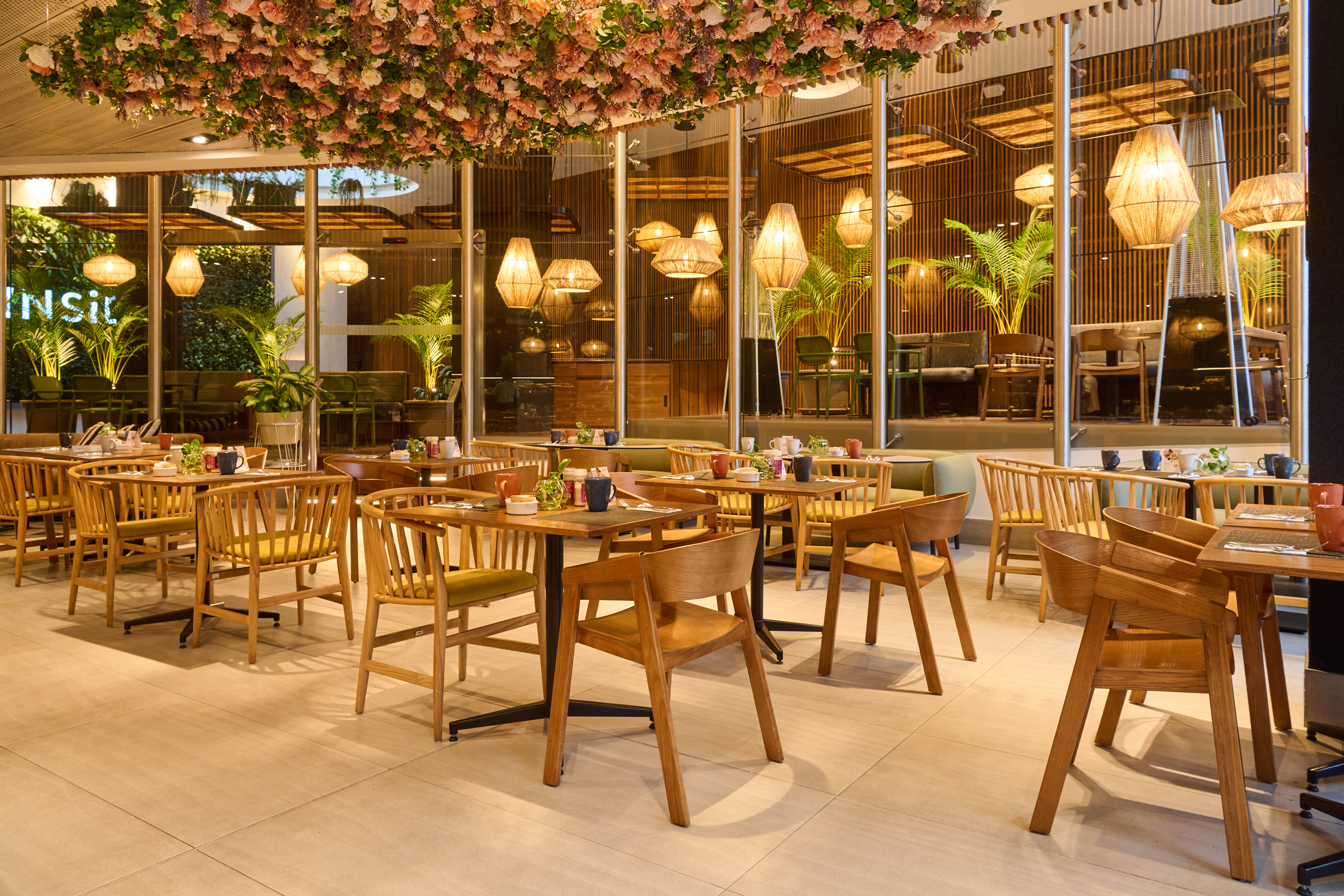 Restaurant dining area with floral ceiling, wooden tables, and woven lights.