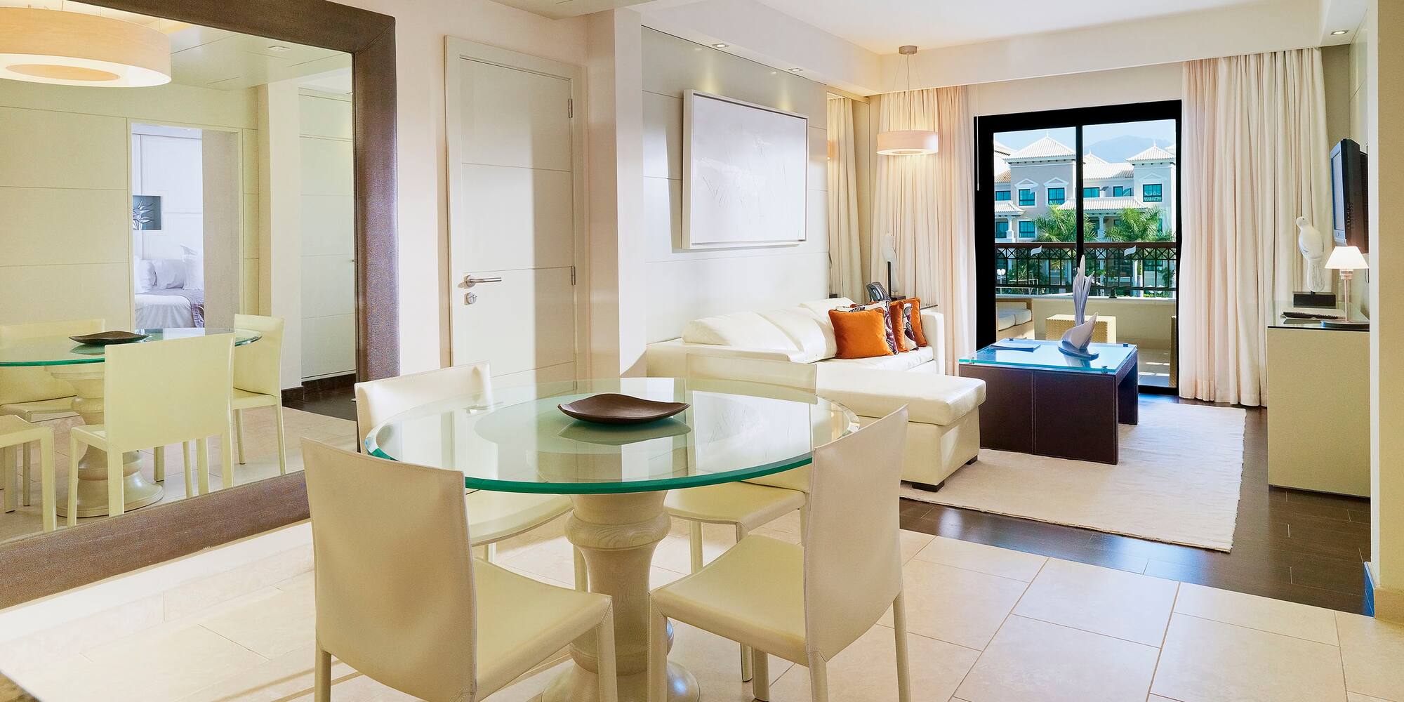 Modern hotel suite living and dining room with white sofa and balcony view.