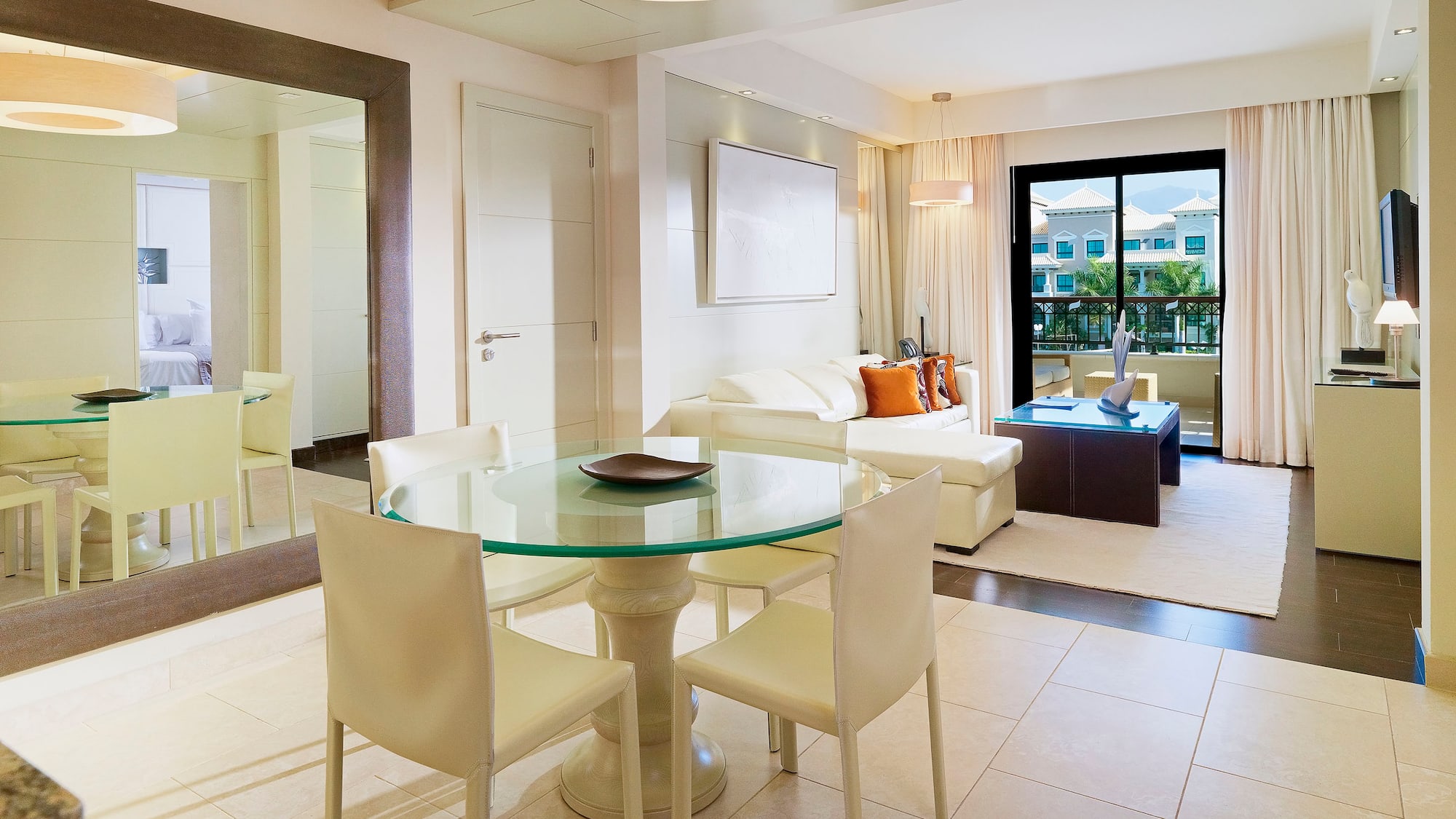 Modern hotel suite living and dining room with white sofa and balcony view.
