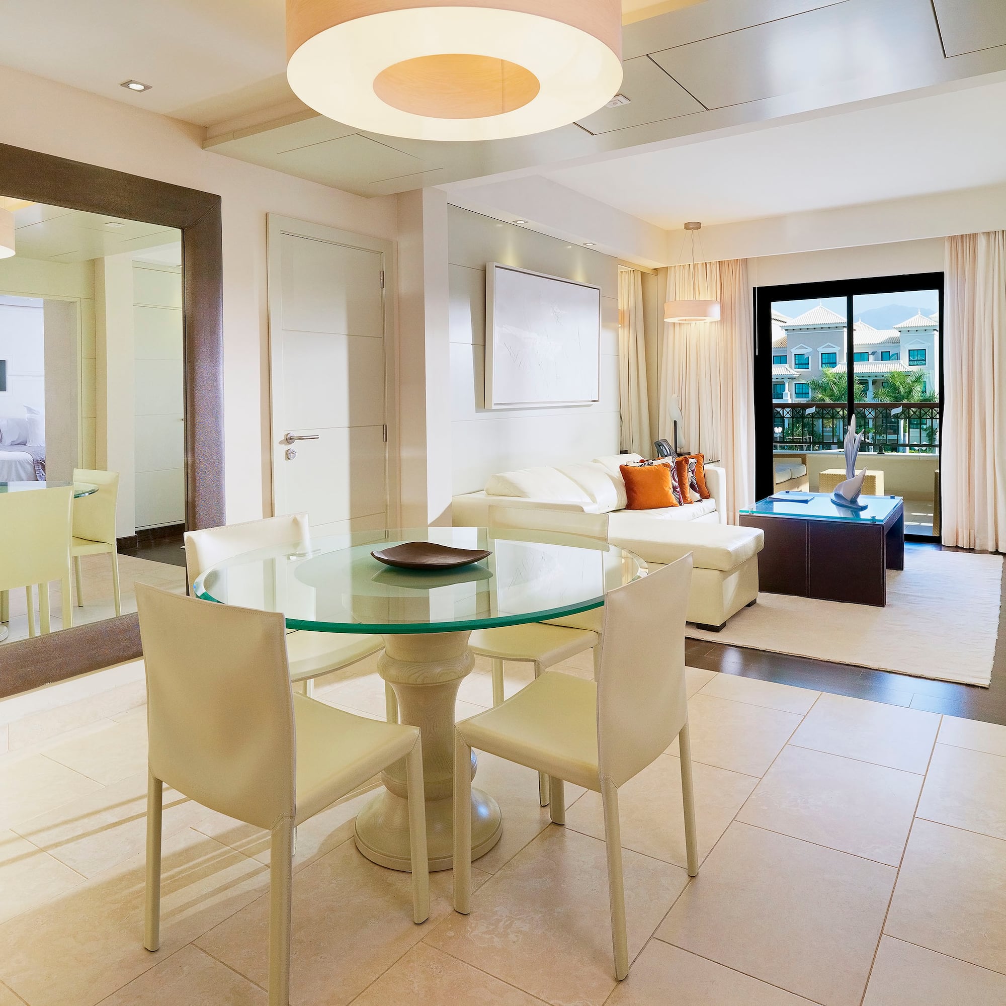 Modern hotel suite living and dining room with white sofa and balcony view.