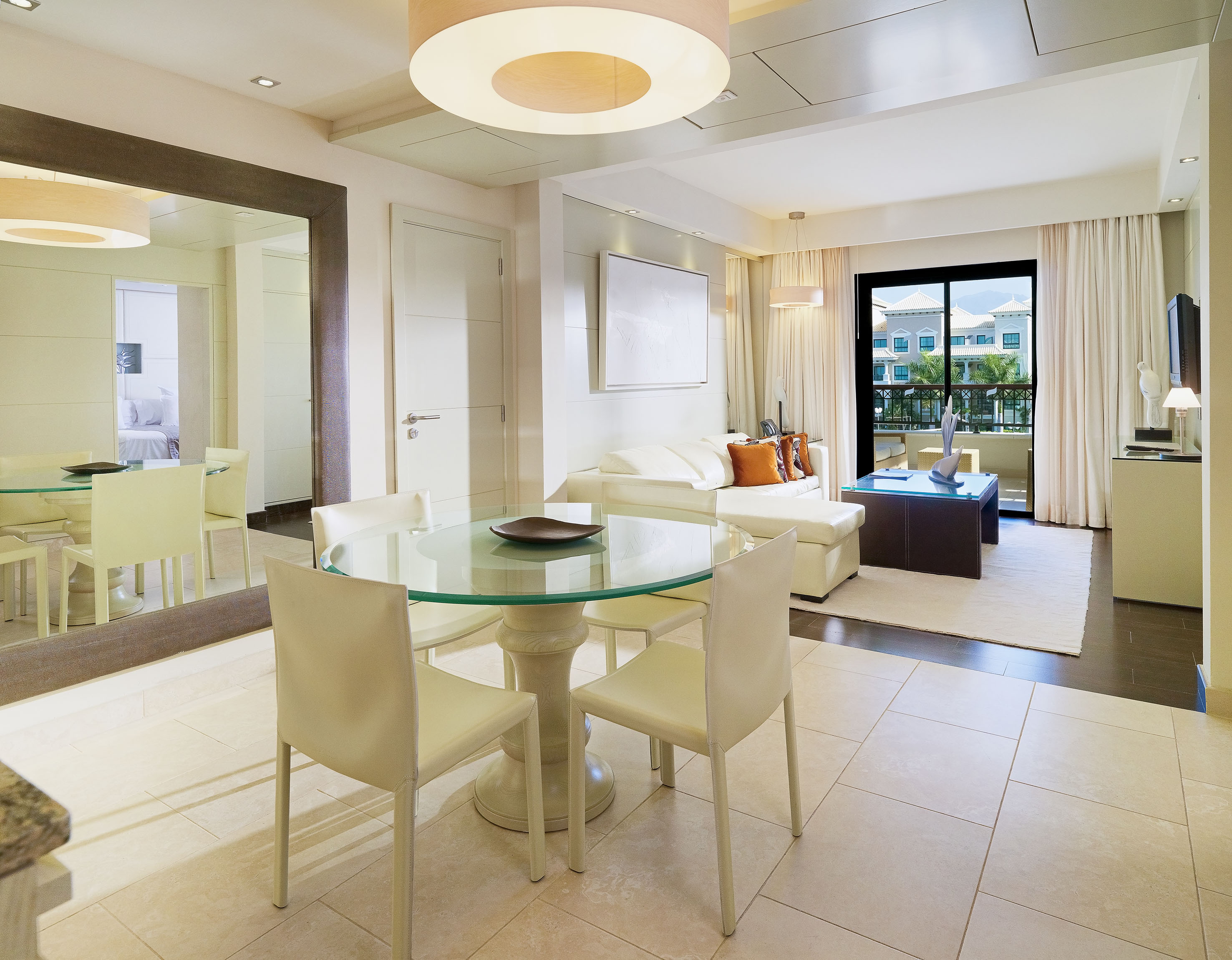 Modern hotel suite living and dining room with white sofa and balcony view.