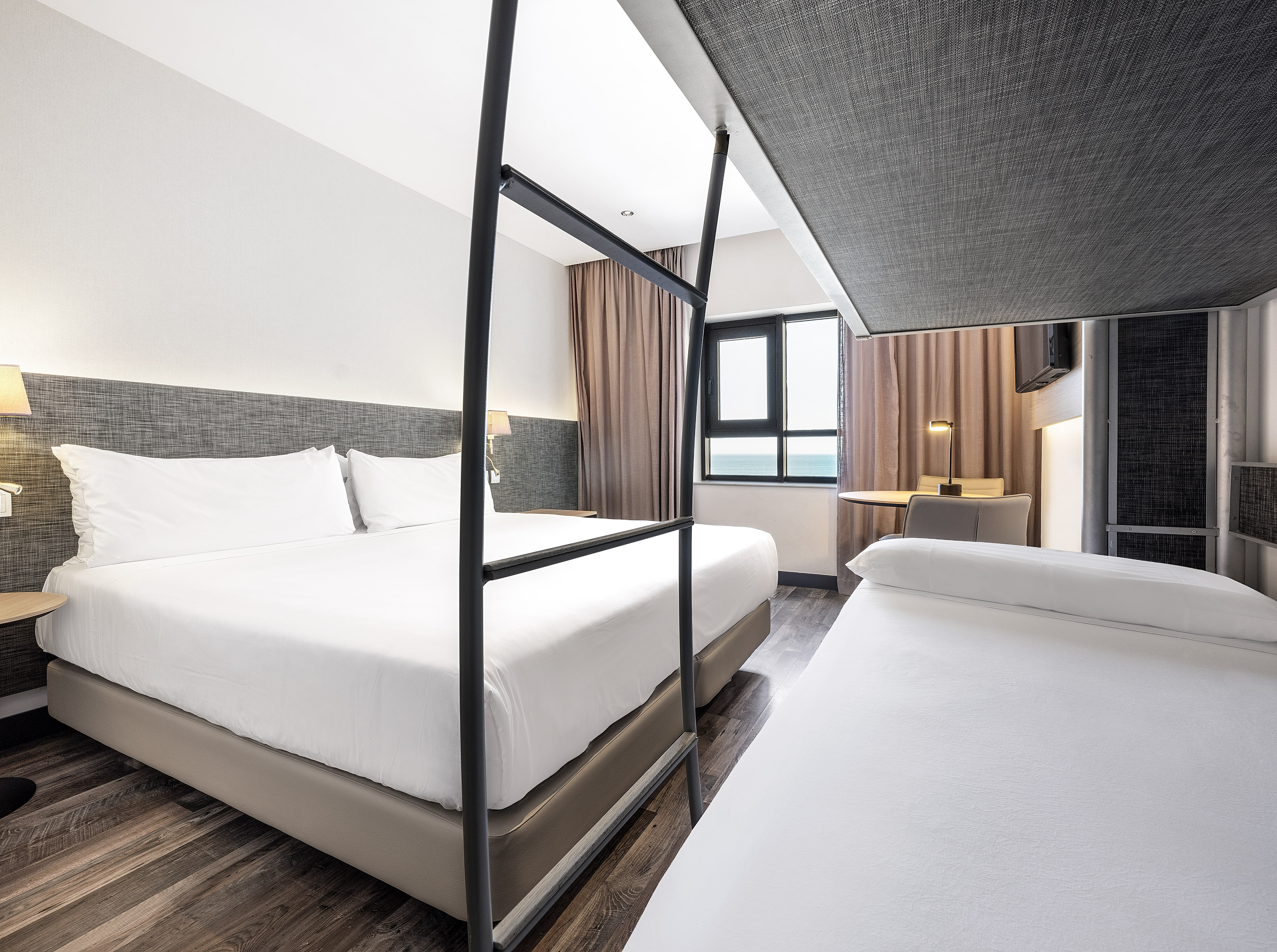 Modern hotel family room with double bed, bunk beds, and sea view window.