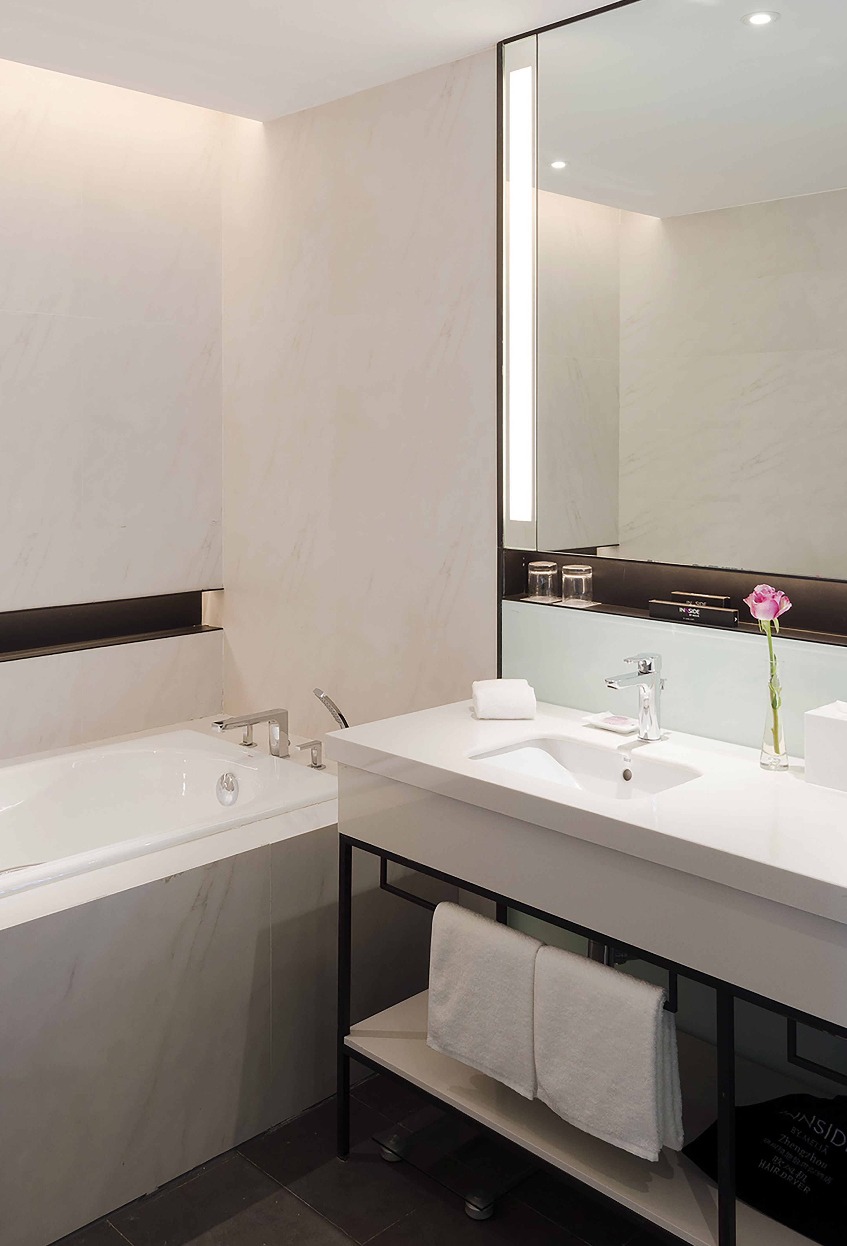 Modern marble bathroom with white bathtub, sink vanity, and illuminated mirror.