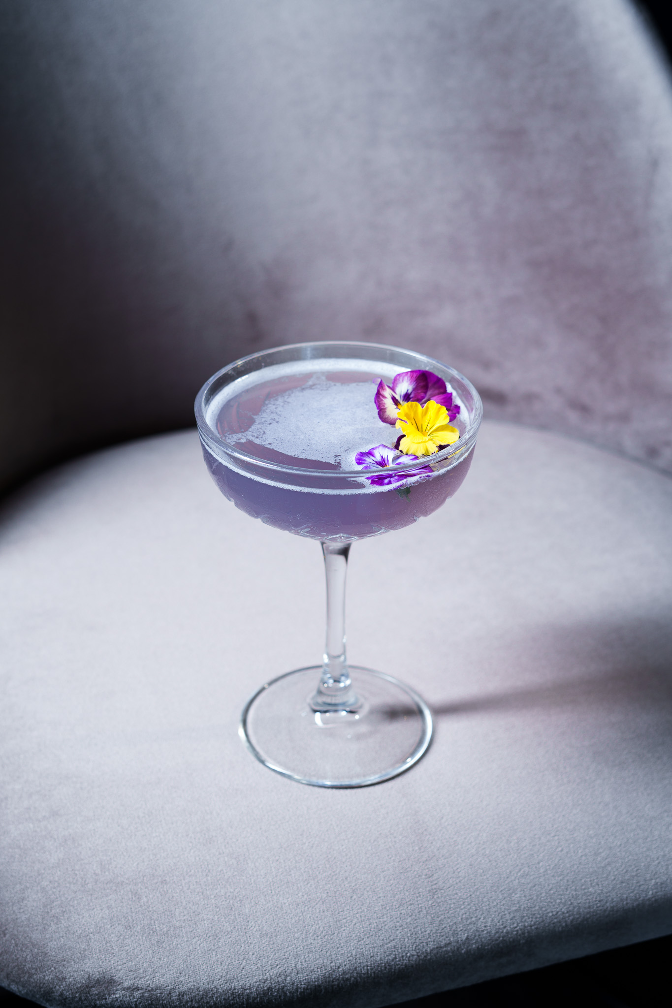 Lavender cocktail with pansy flowers in a coupe glass.