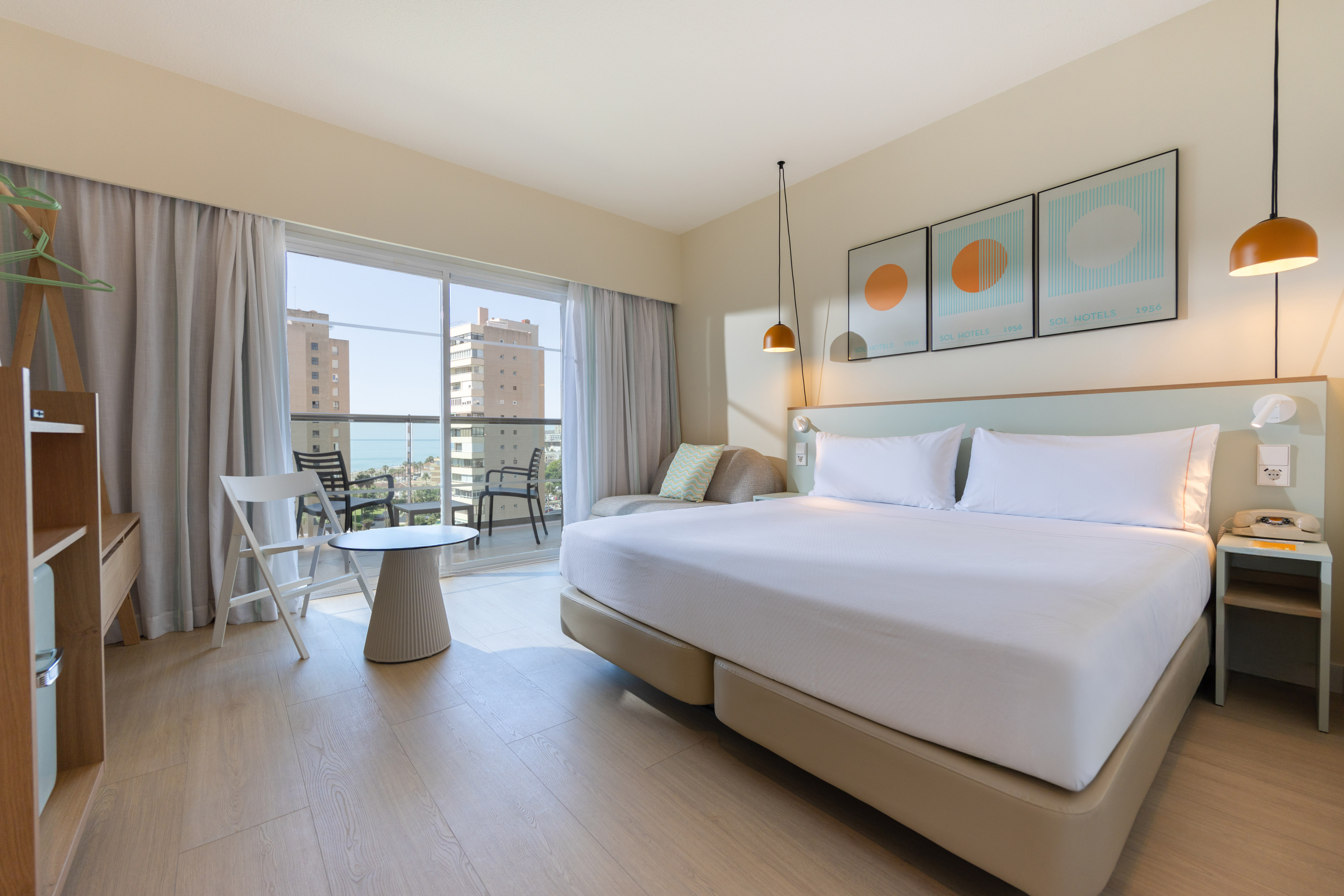 Modern hotel room with balcony ocean view, large bed, and light wood floor.