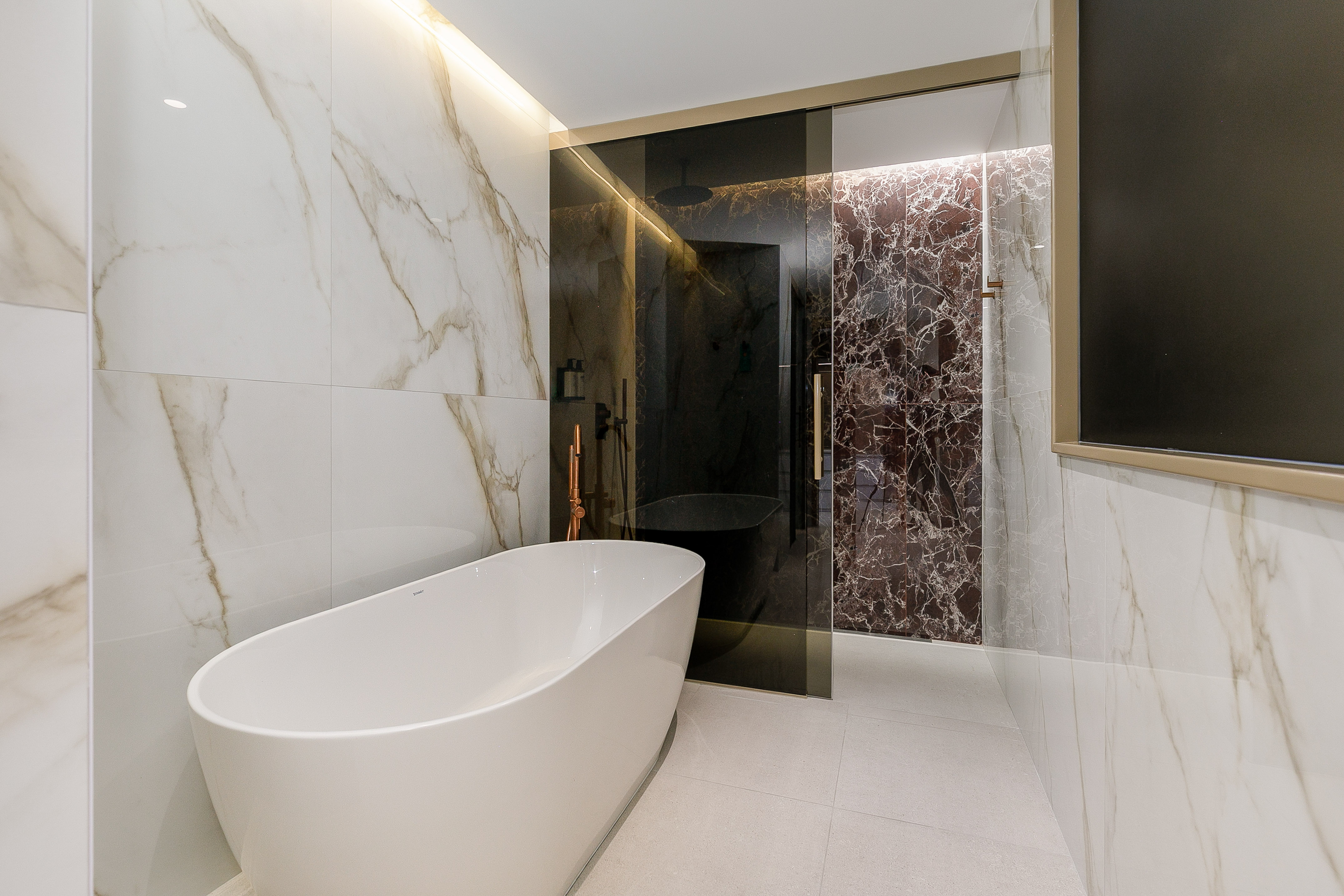 Modern bathroom: freestanding tub, marble walls, dark glass shower.