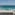 Balcony overlooking turquoise ocean, white walls, and glass railing.