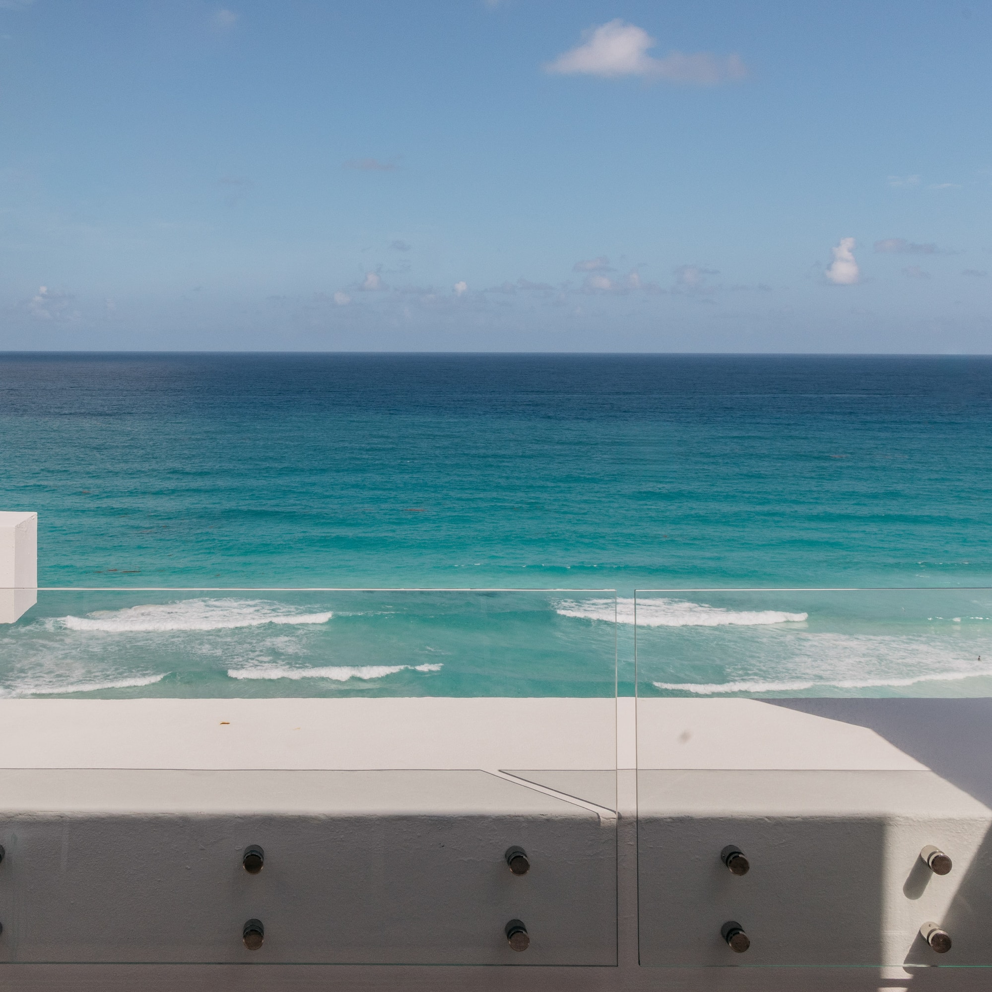 Balcony overlooking turquoise ocean, white walls, and glass railing.